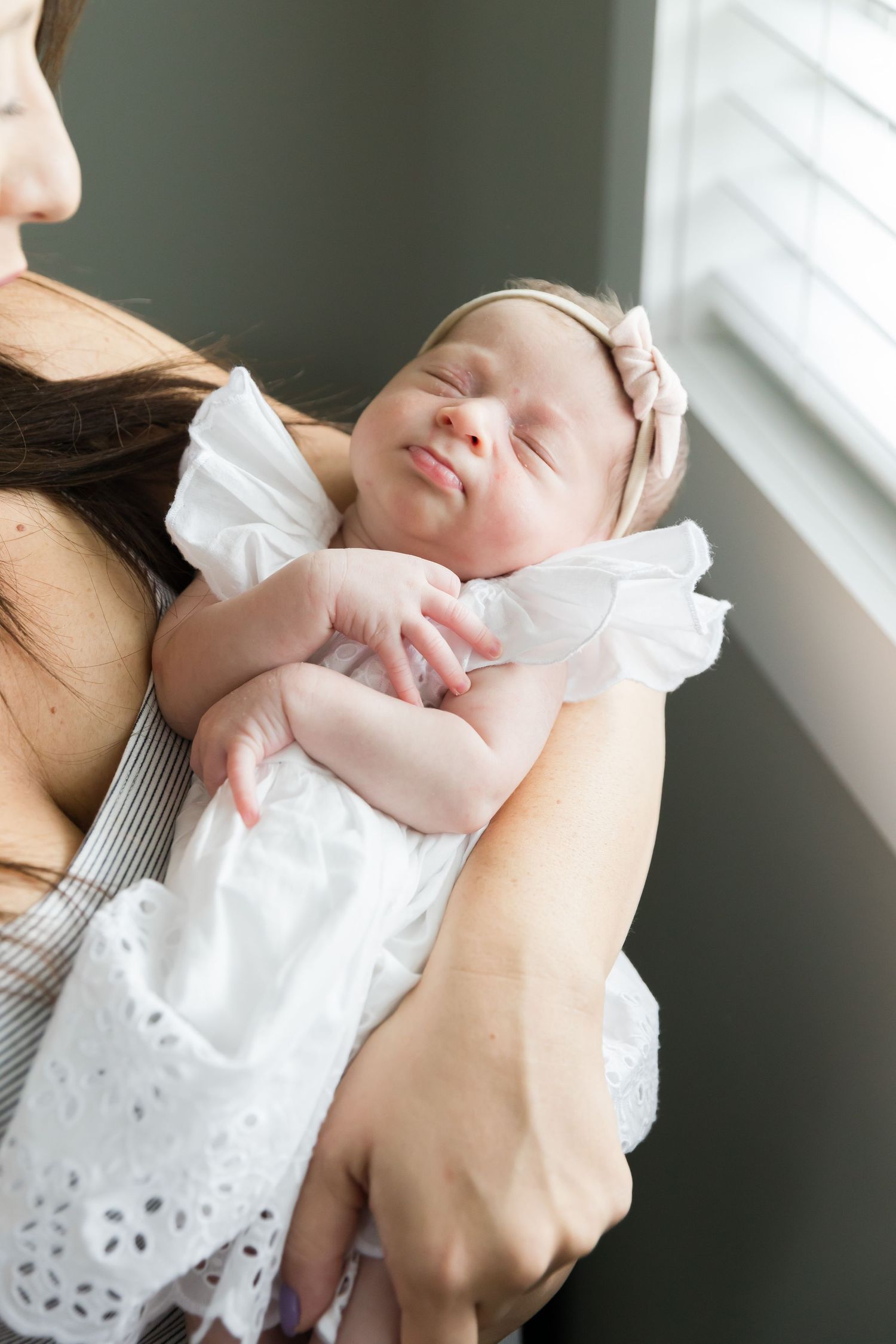 Sleeping baby in white dress being cradled near window.