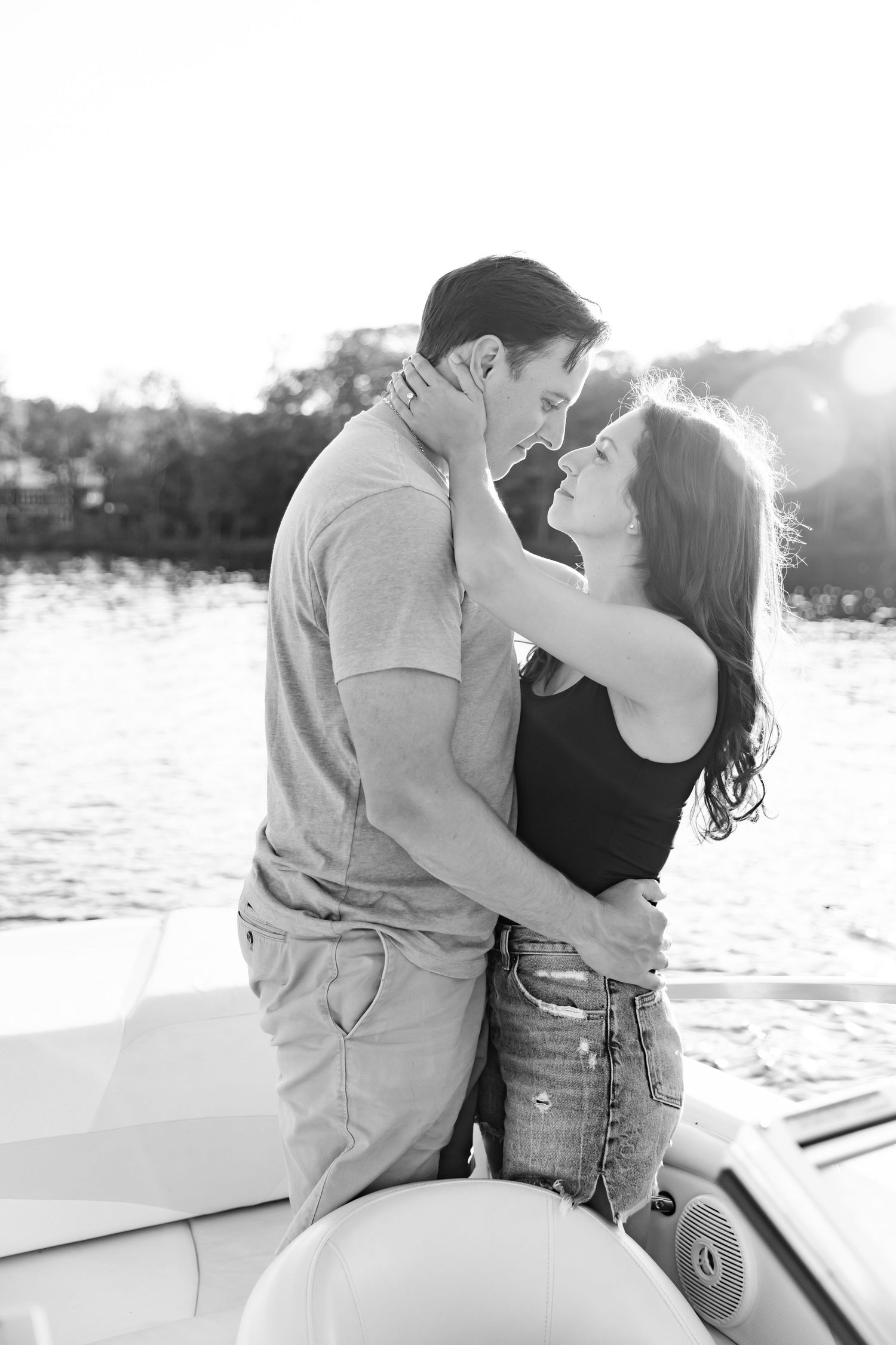 Black and white photo of couple embracing on boat deck at sunset.