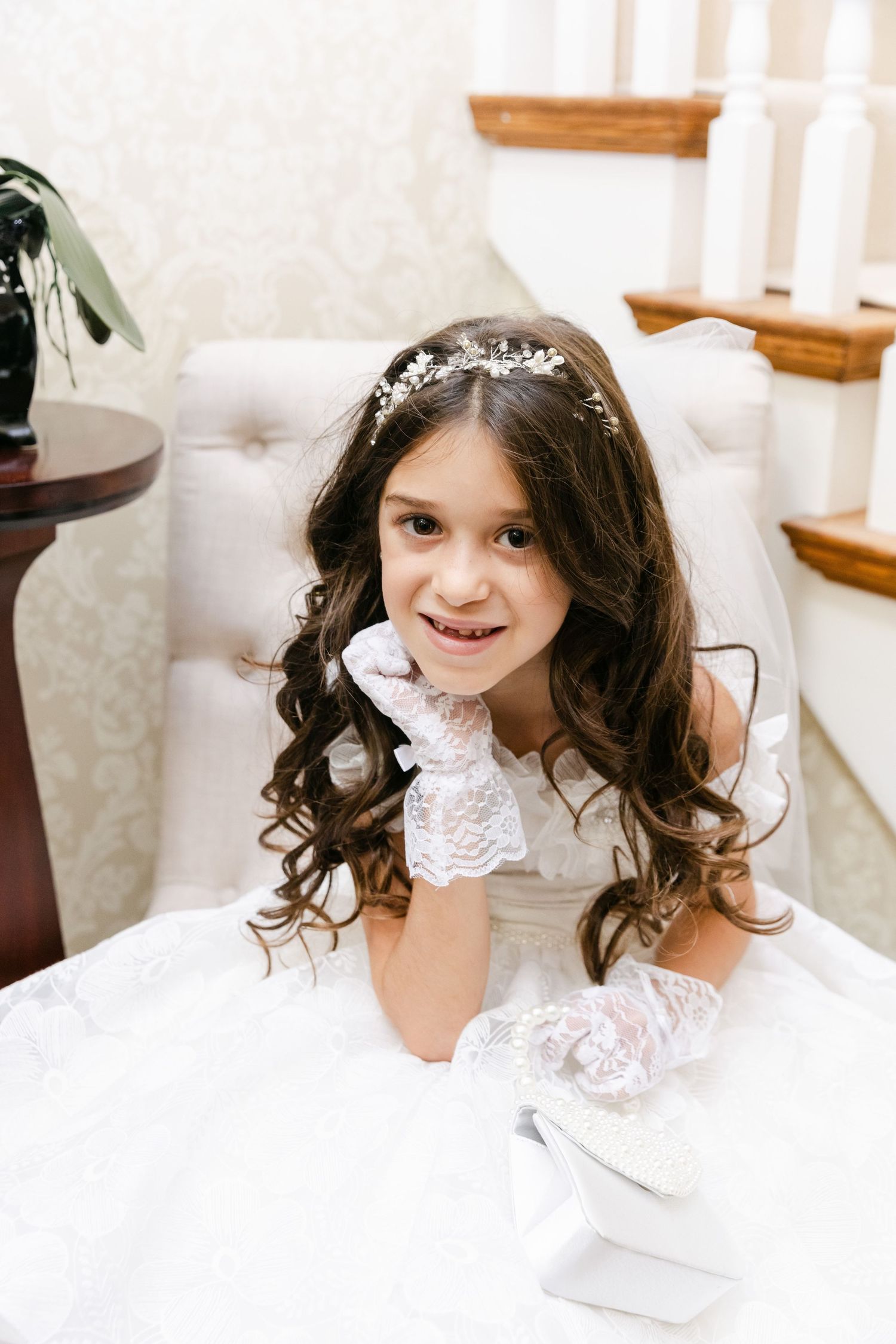 White baptism dress with lace details and sparkly tiara photographed indoors.