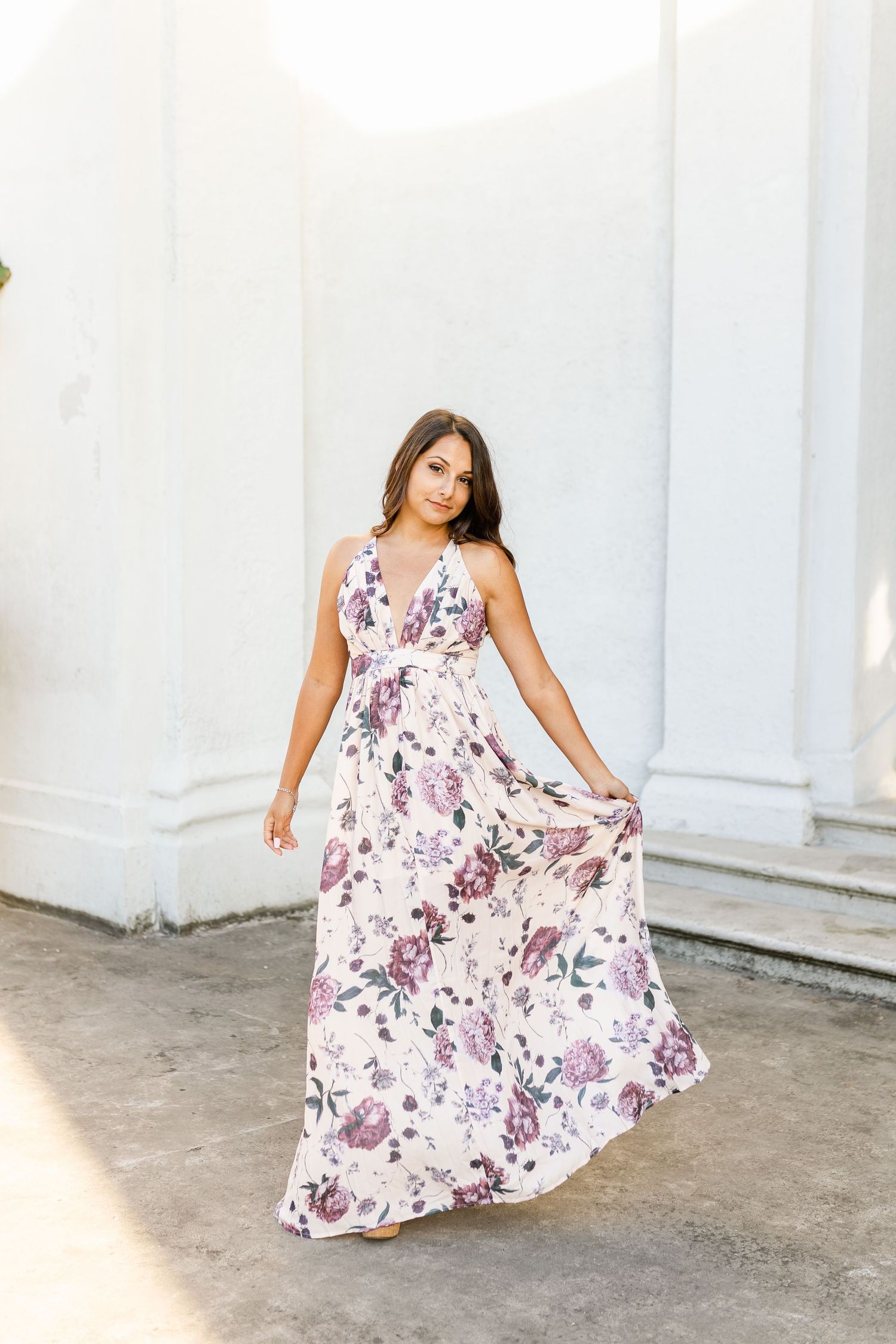Woman in white and purple floral maxi dress posing elegantly against white wall.