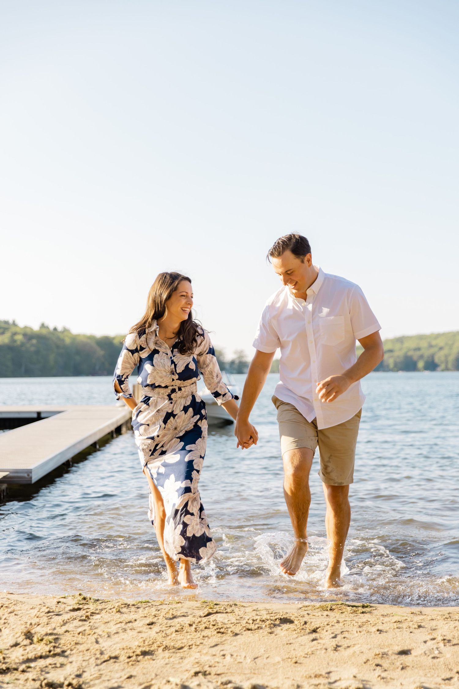 A couple splashes through the water along a lakeside beach on a bright summer day.