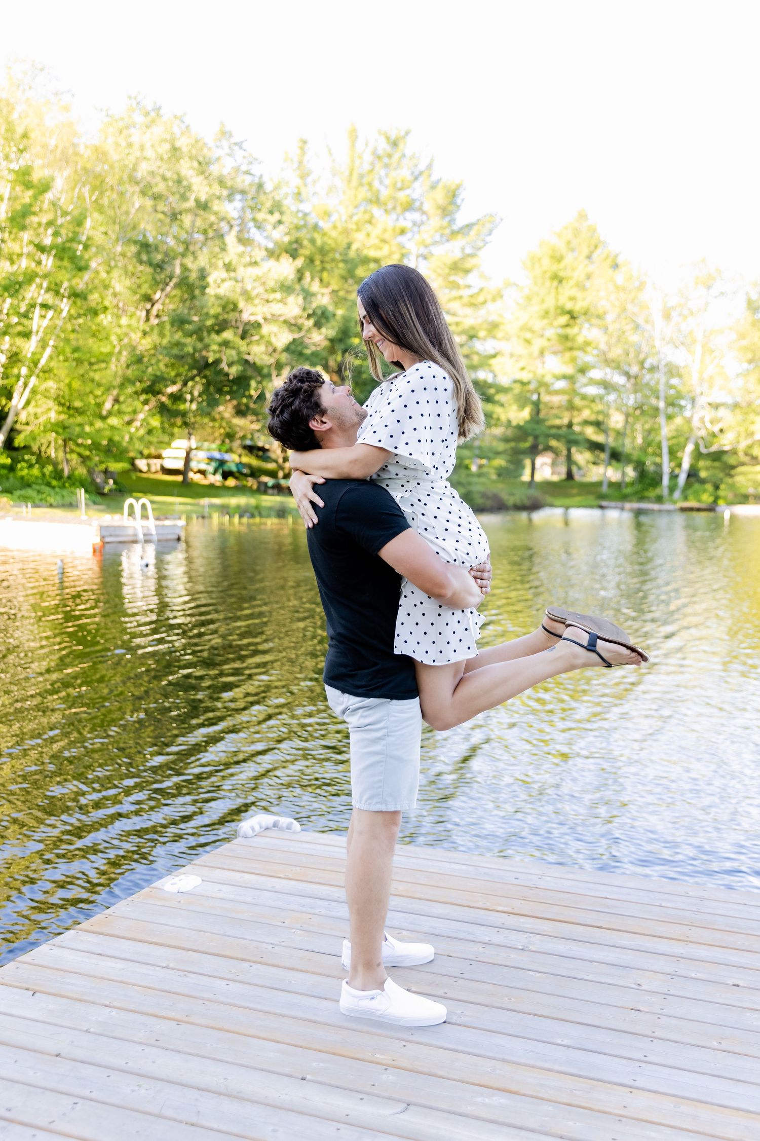 Playful lift pose on wooden dock with lake and trees in background.