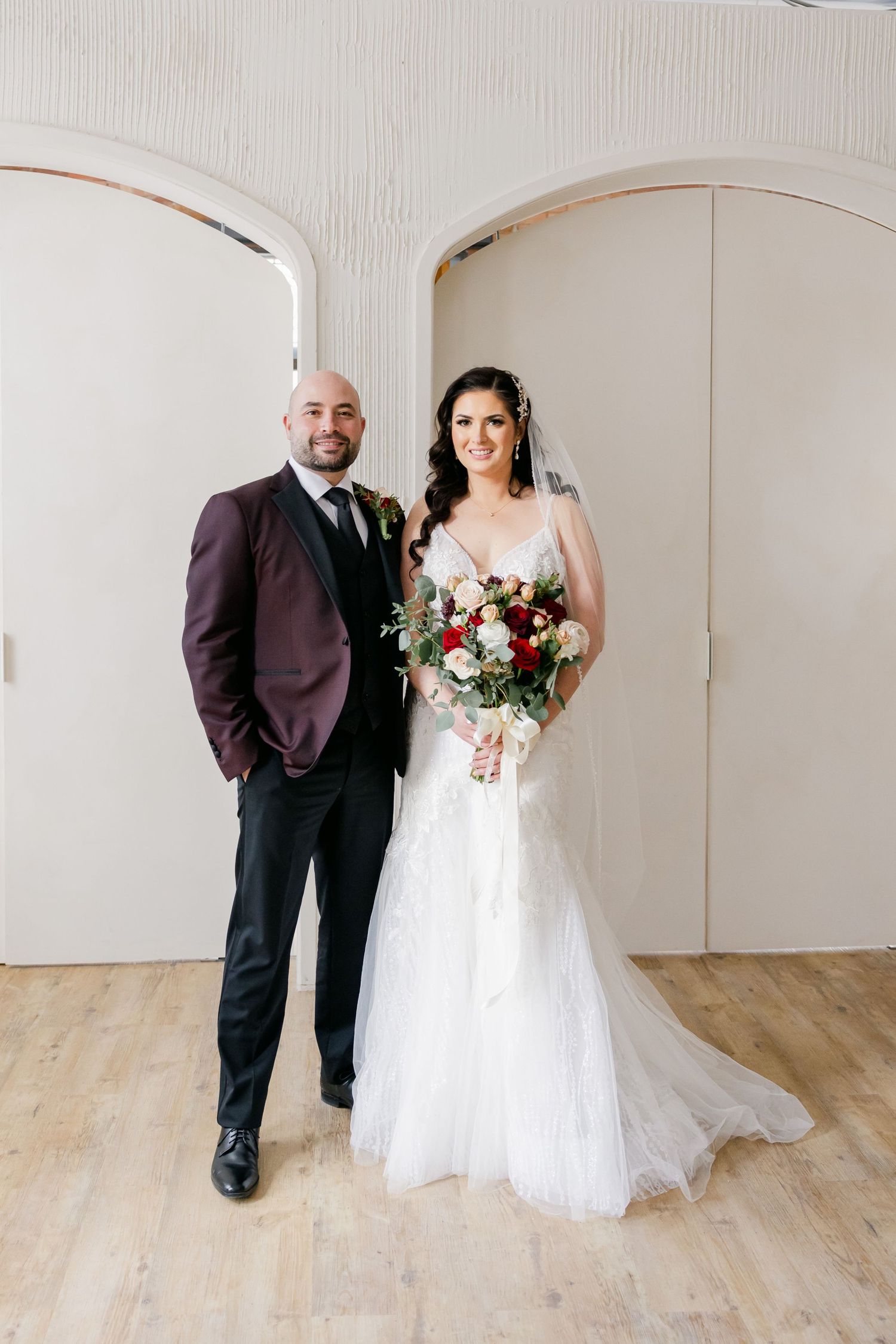 Elegant wedding portrait with couple standing against white arched wall.