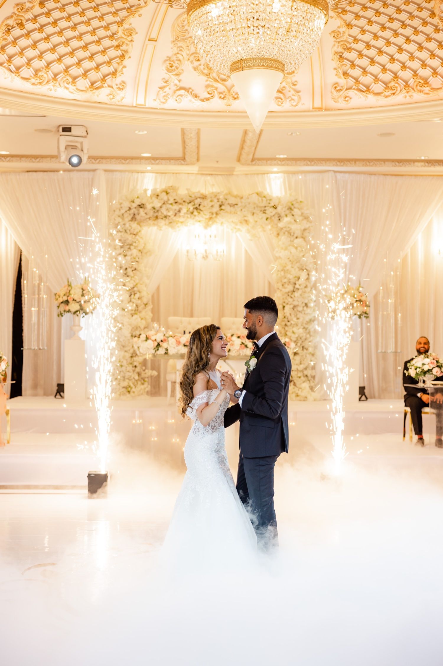 Newlyweds share romantic dance moment with sparklers and fog effects in luxurious venue.