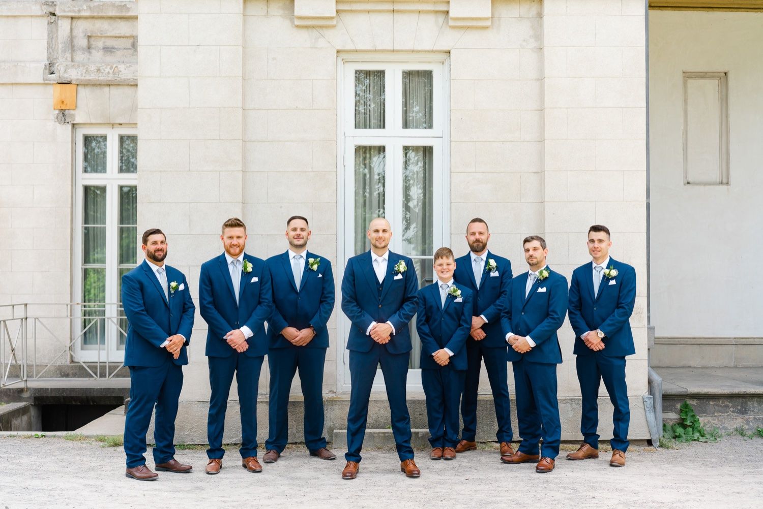 Groomsmen in matching navy suits and brown shoes line up for formal portrait.