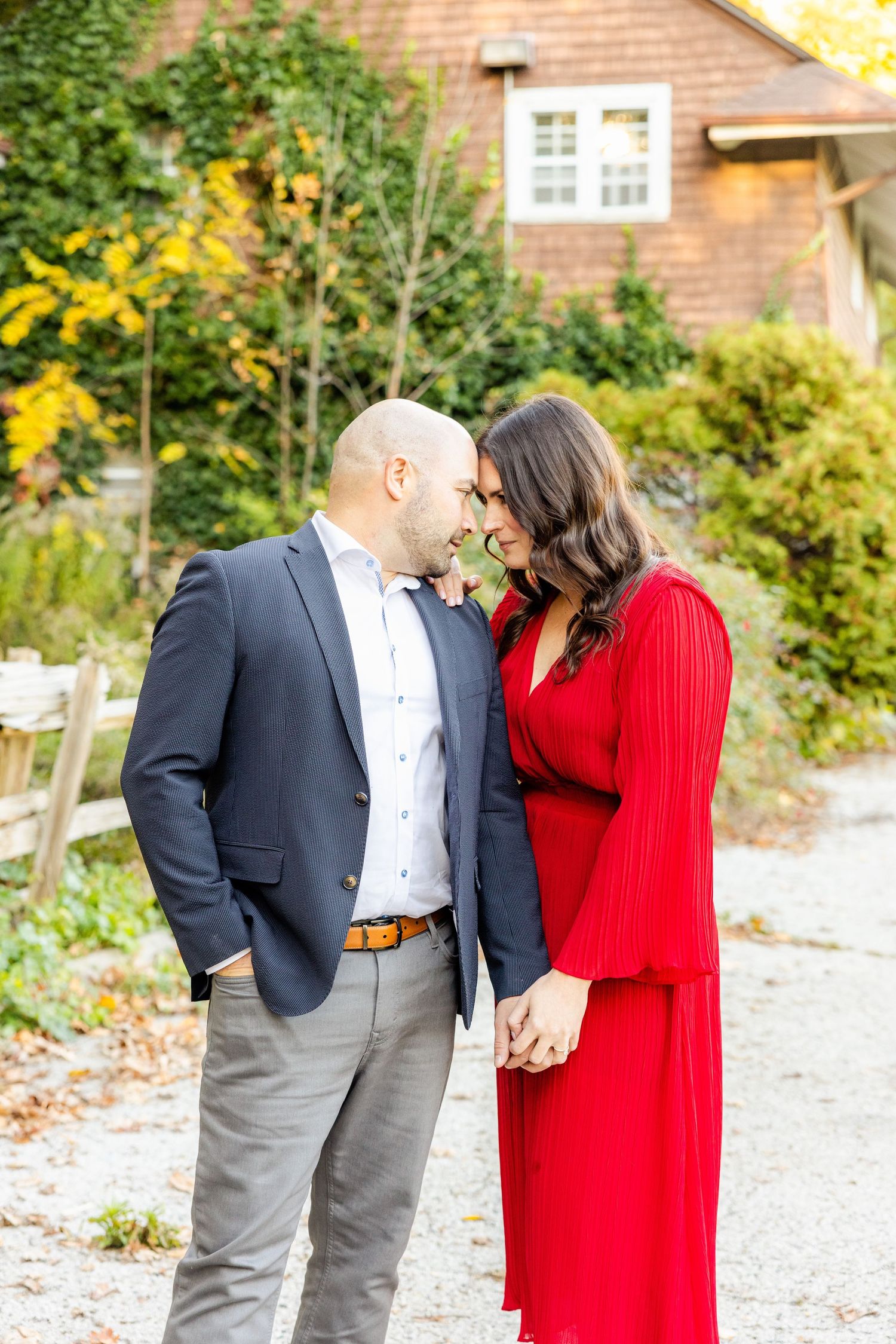 Sweet intimate moment between couple against brick house with fall foliage.