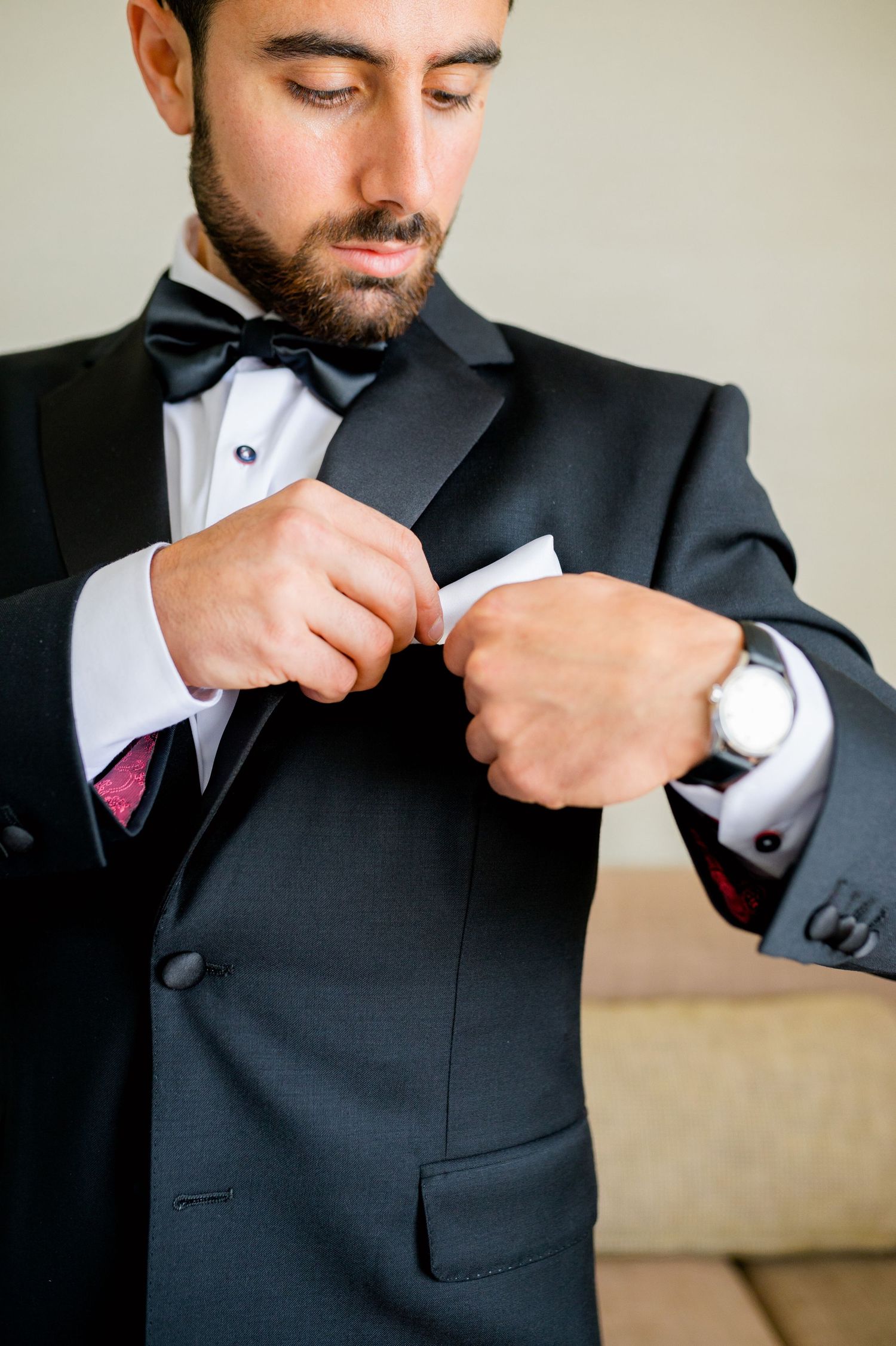 Close-up shot of hands adjusting formal tuxedo jacket and accessories.