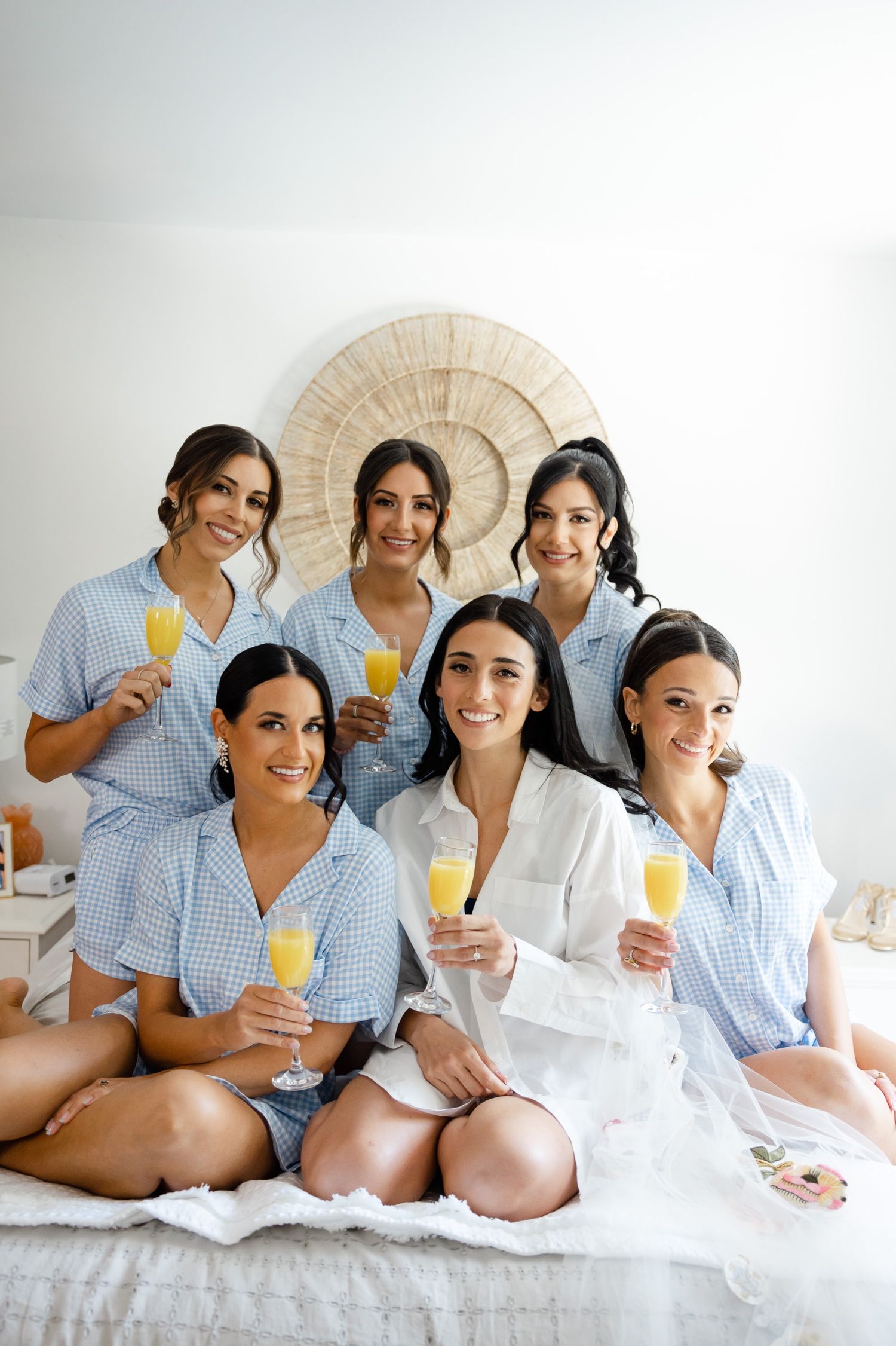 Wedding party wearing matching blue striped pajamas enjoying mimosas on bed.