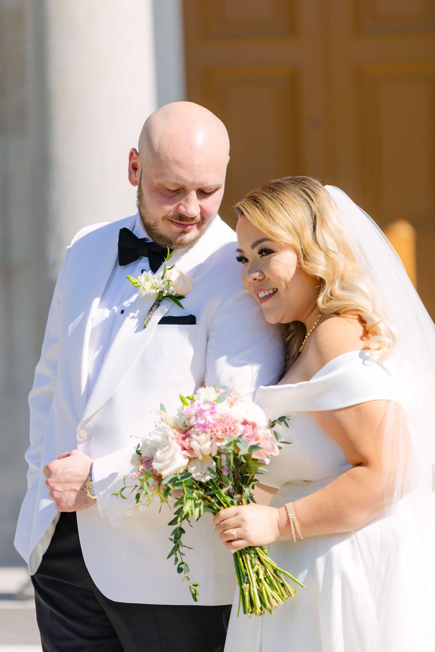 Newlyweds share intimate moment while holding pink and white floral bouquet.