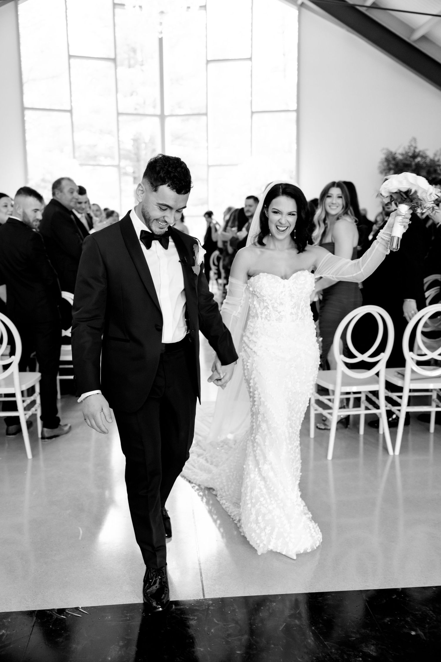 A black and white photo capturing a joyful wedding exit down the aisle.