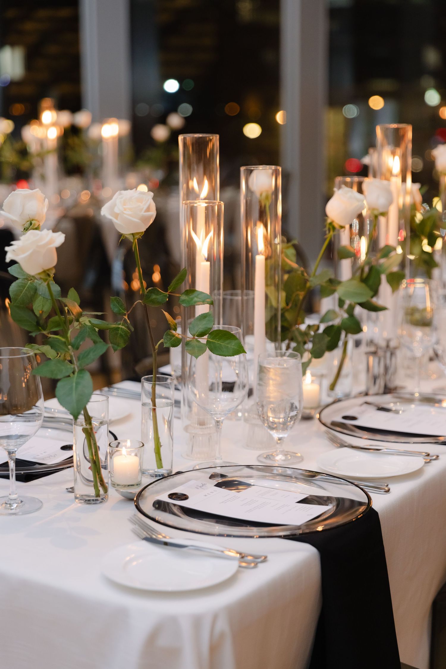 Elegant table setting with white roses, glass candleholders, and black and white place settings.