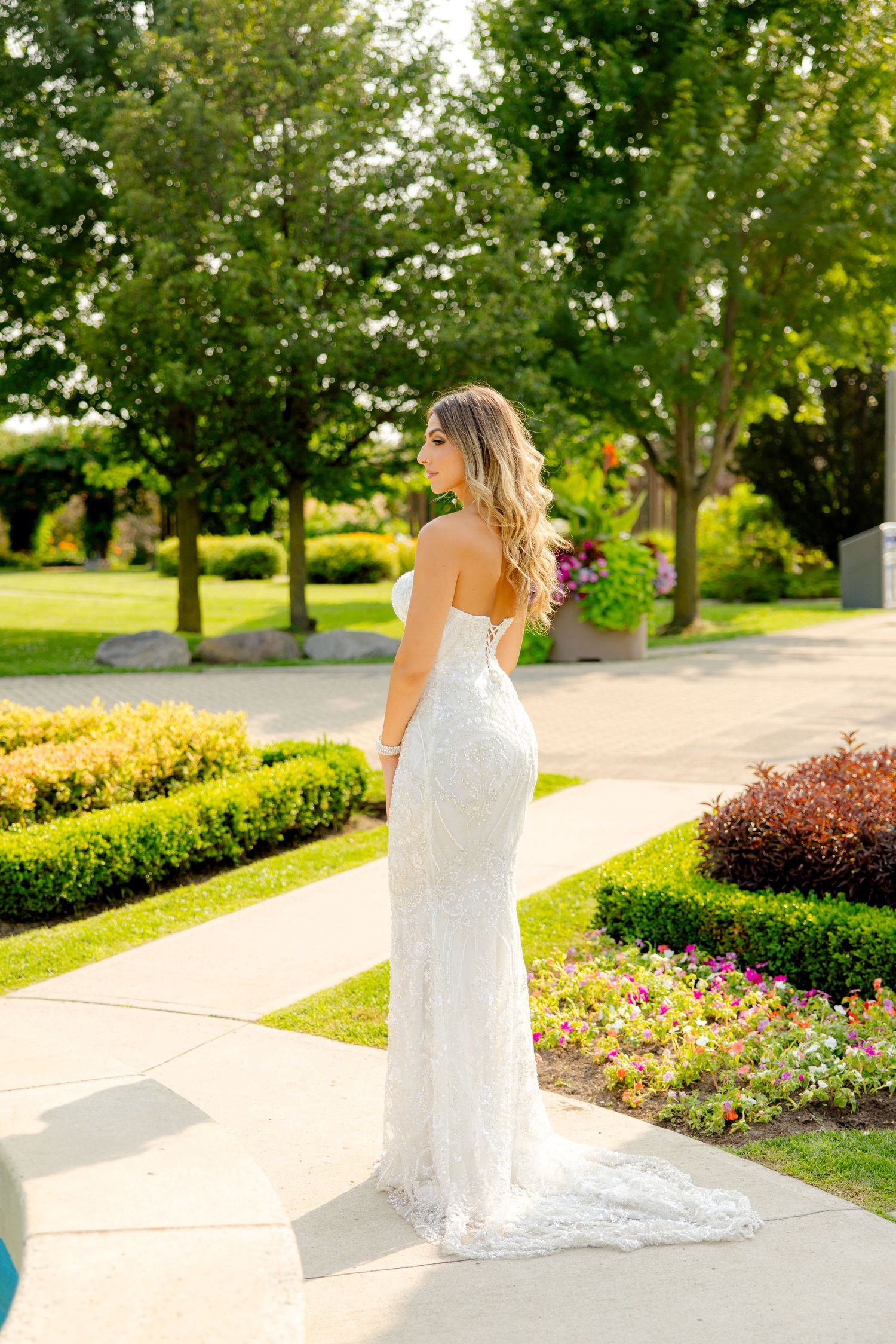 Elegant bride in fitted lace gown poses in sunlit garden setting with flowing train.
