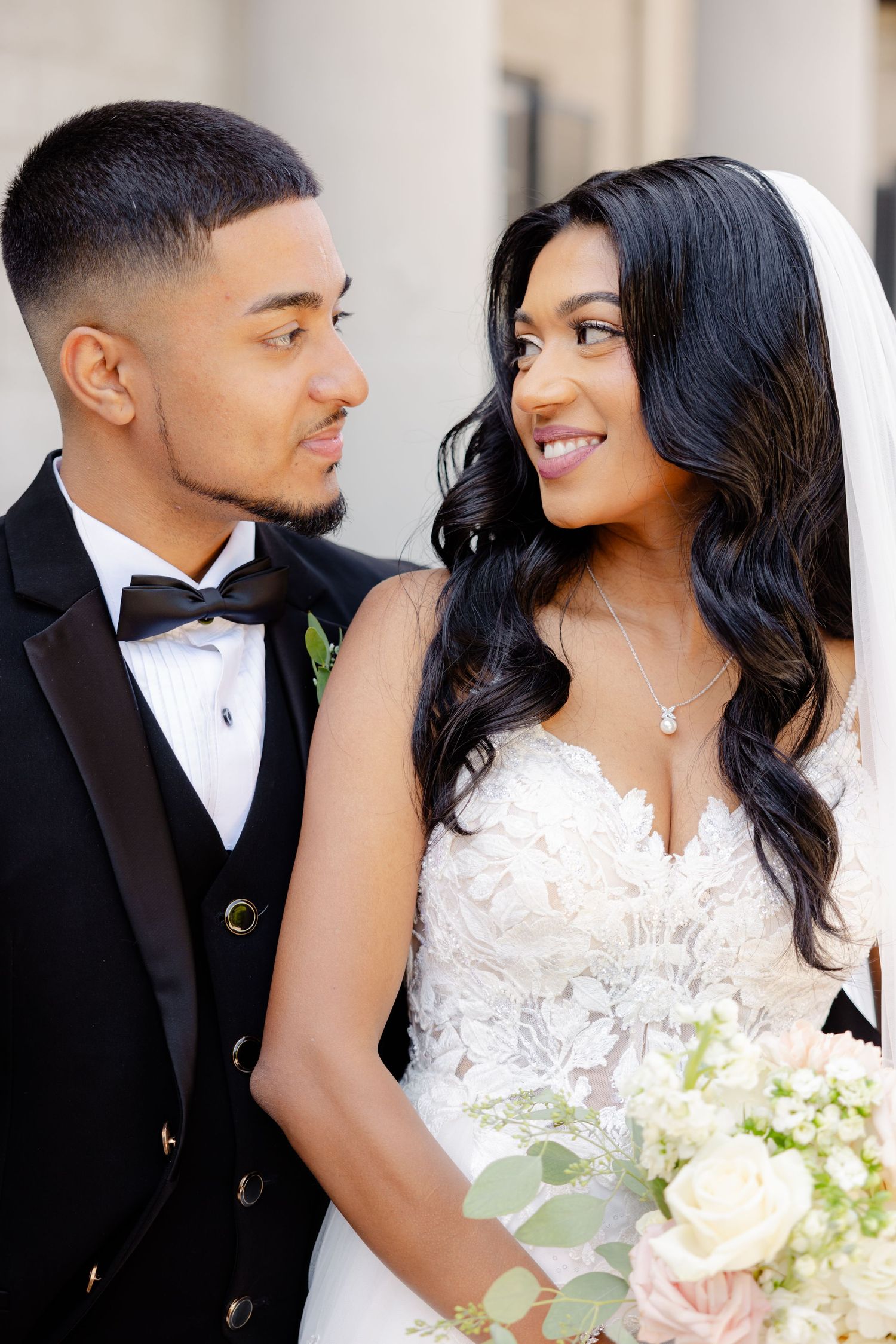 Close up portrait of couple sharing loving glance with bride holding fresh floral bouquet.