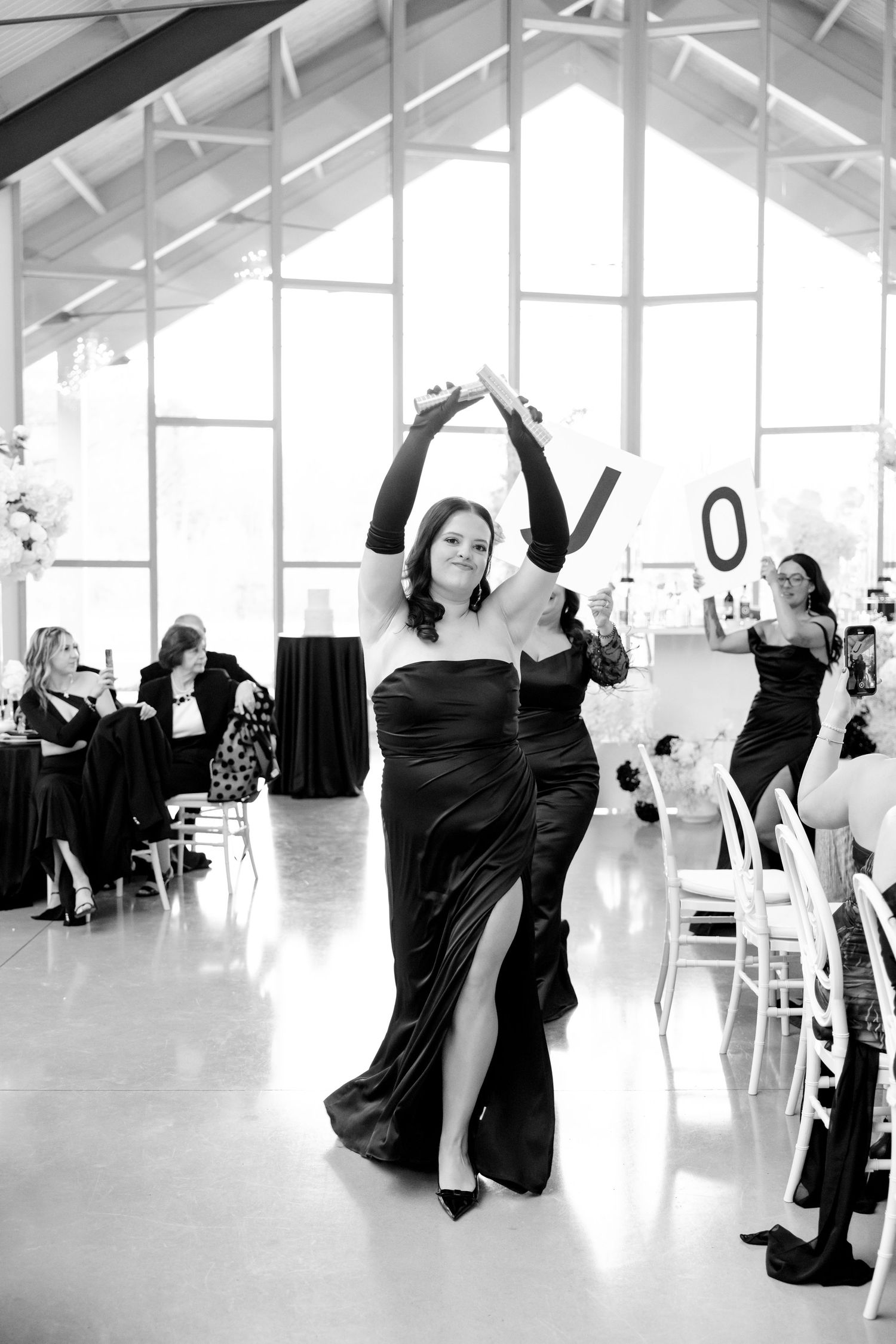 A wedding guest in a black dress dances joyfully at the reception.