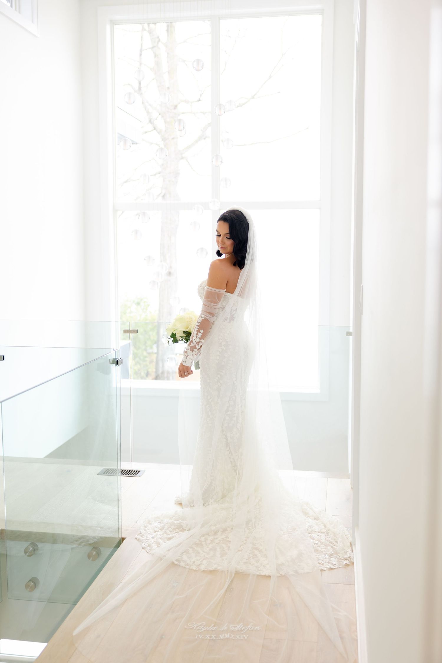 A side profile bridal portrait in a bright hallway with glass railings showcasing an elegant lace wedding gown.
