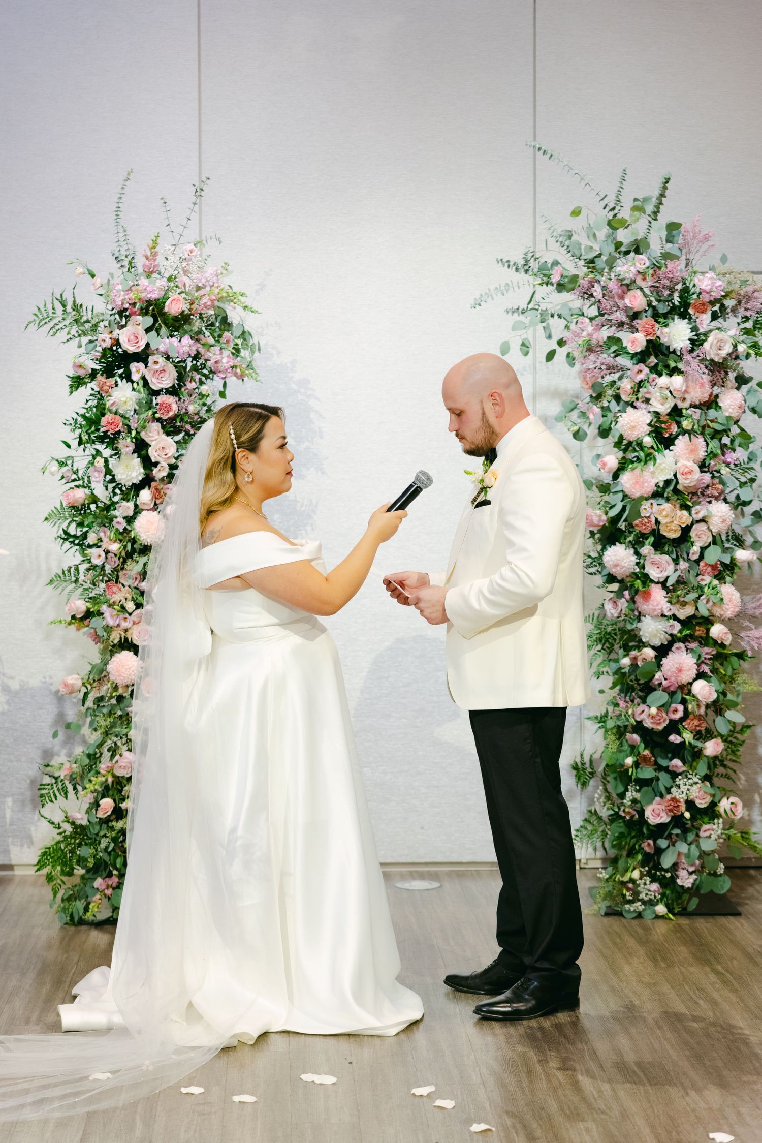 Couple exchanging vows under beautiful floral arches with pink roses and greenery during wedding ceremony.