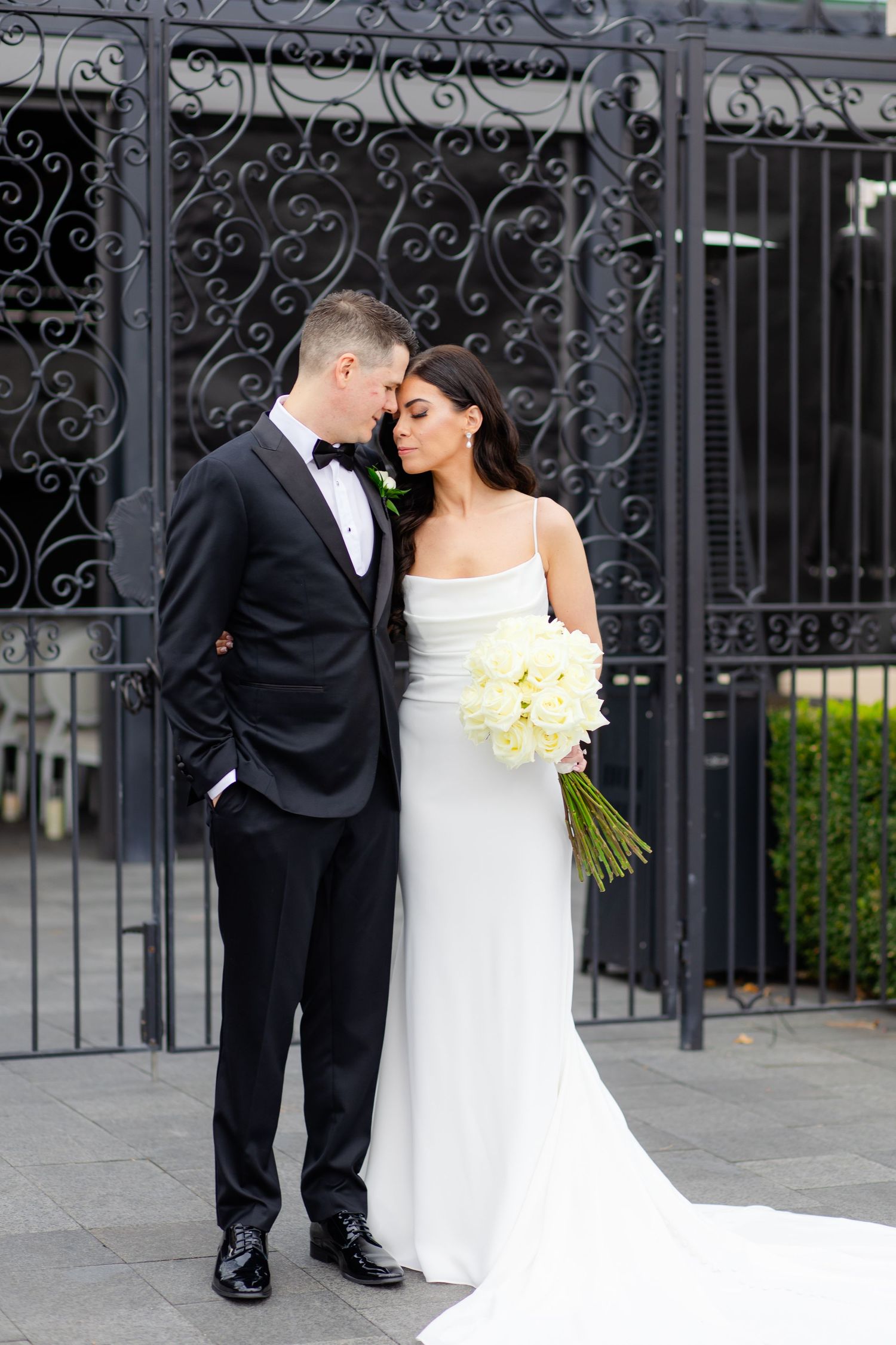 Elegant couple in wedding attire pose before an ornate wrought iron gate.