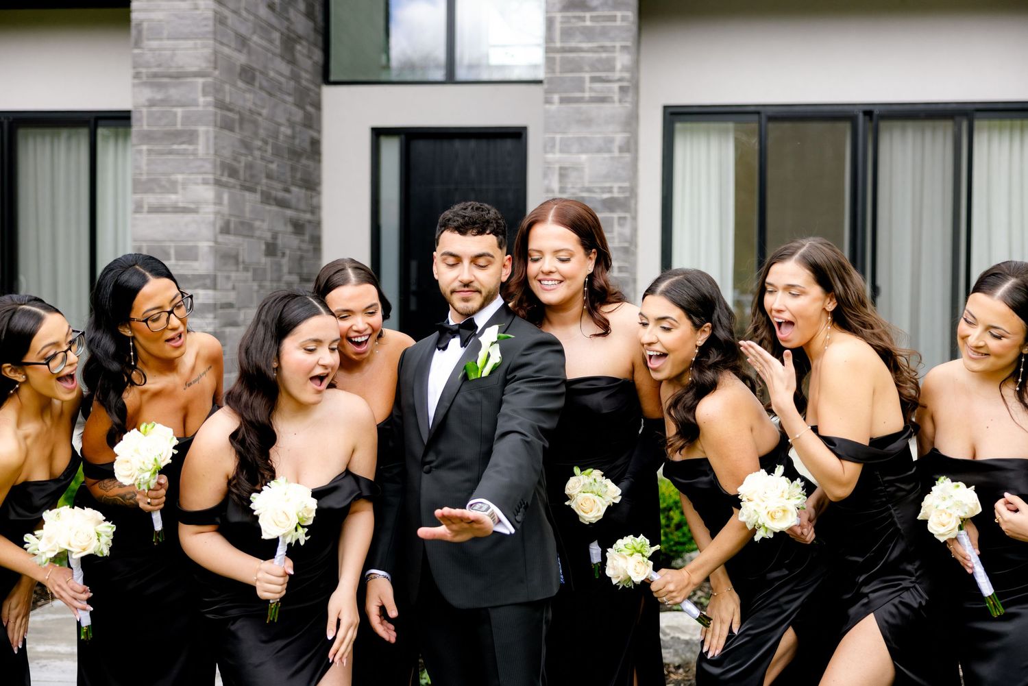 Joyful wedding party in black attire shares laughs during outdoor photo session.