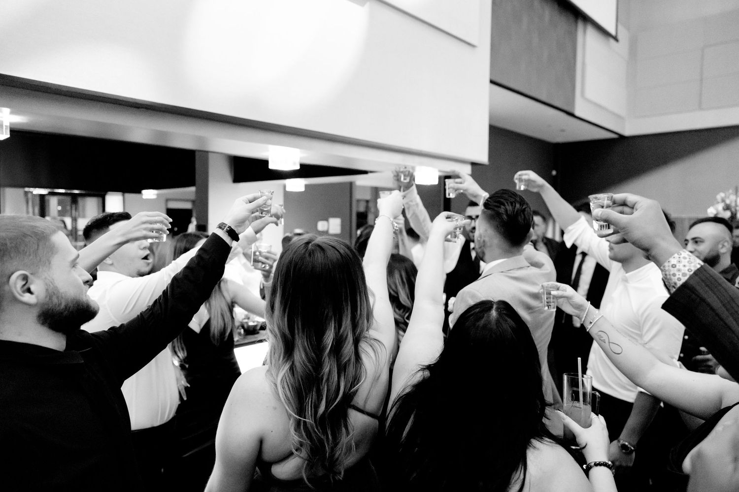 Black and white photo of wedding celebration with crowd raising drinks in toast.