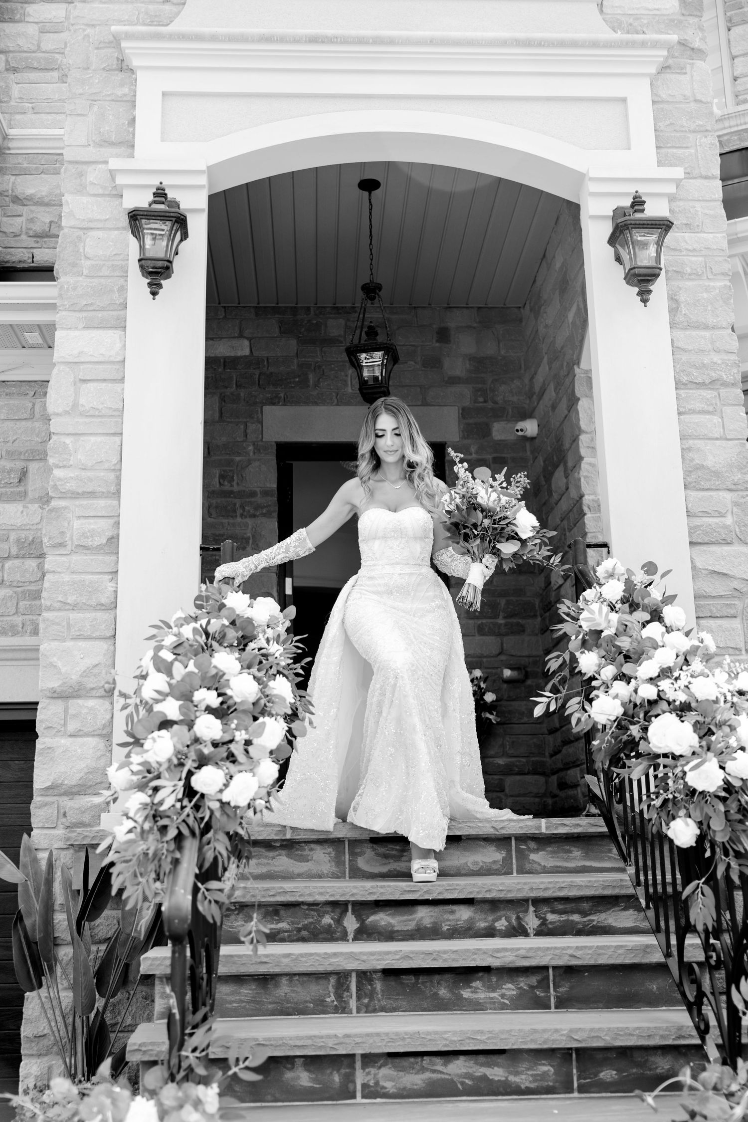 Black and white photo of grand entrance with floral arrangements and stone architecture.