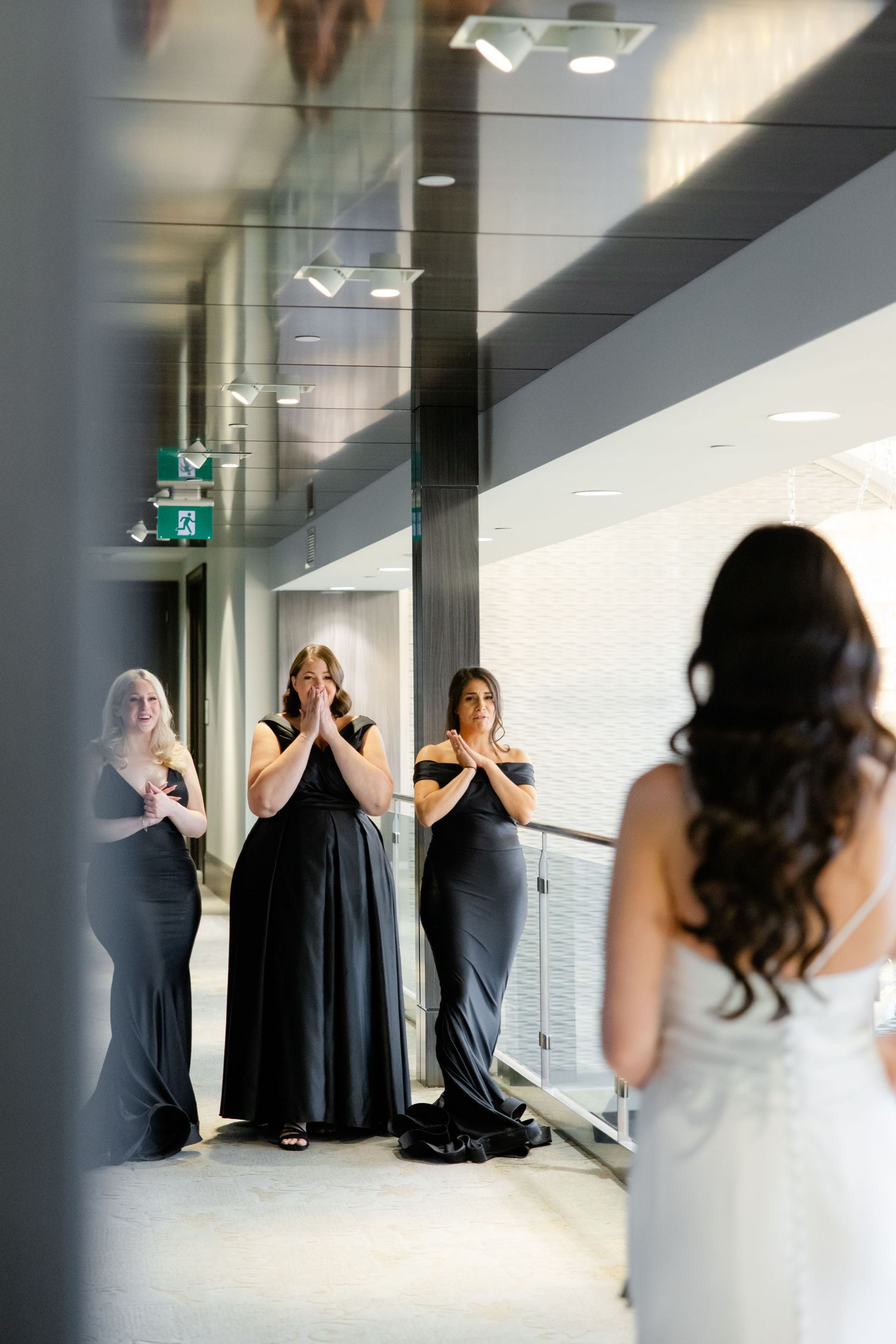 Emotional bridesmaids reaction during first look with bride in a modern venue hallway.