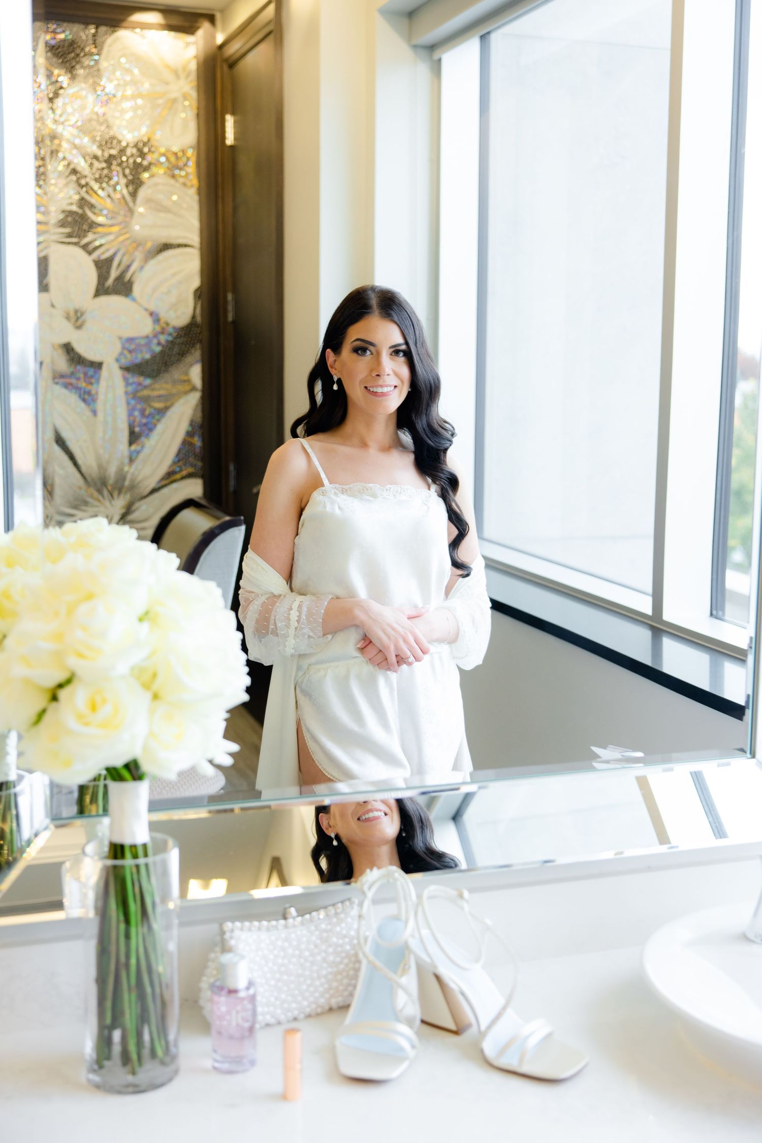 Bride in white robe during wedding preparations with yellow floral bouquet in modern setting.
