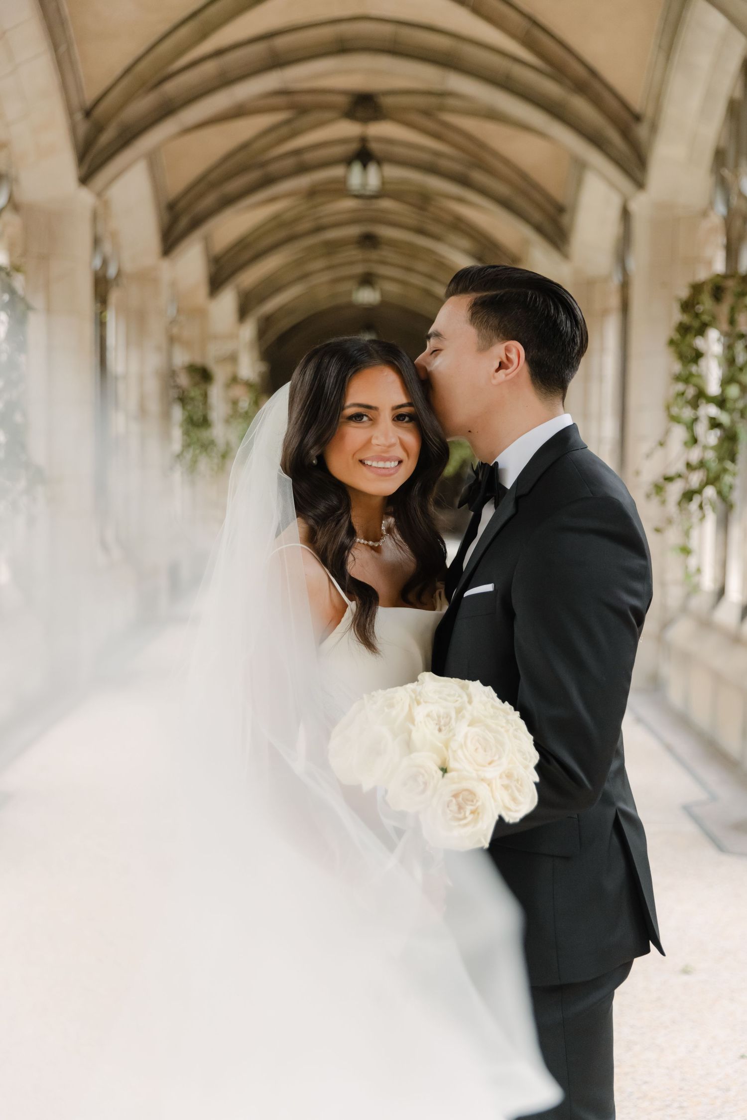 Elegant wedding portrait in stone corridor with natural light streaming through arched windows.