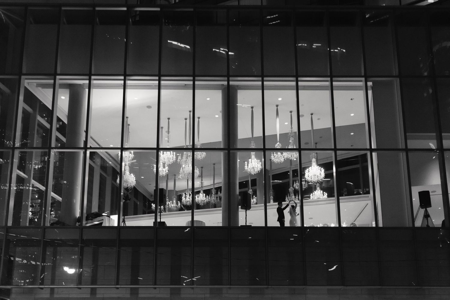 Modern glass building facade lit from within at night showing silhouettes of people.