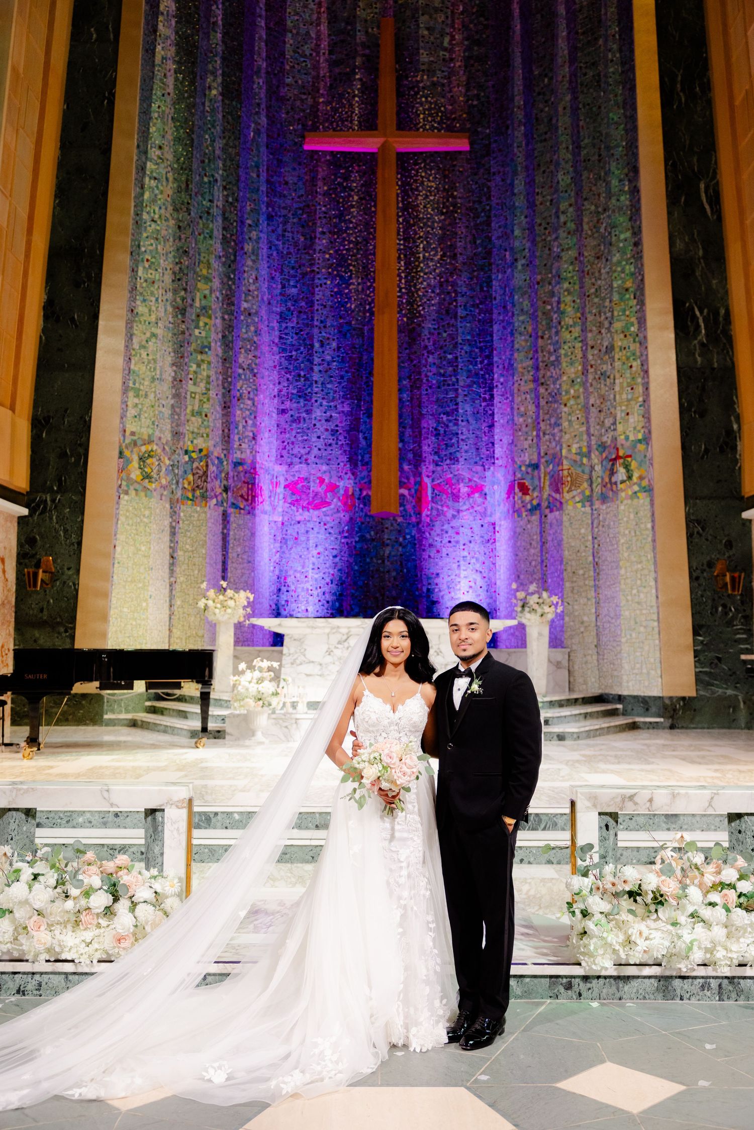 A wedding ceremony in a church with a dramatic purple-lit cross and elegant floral decorations.