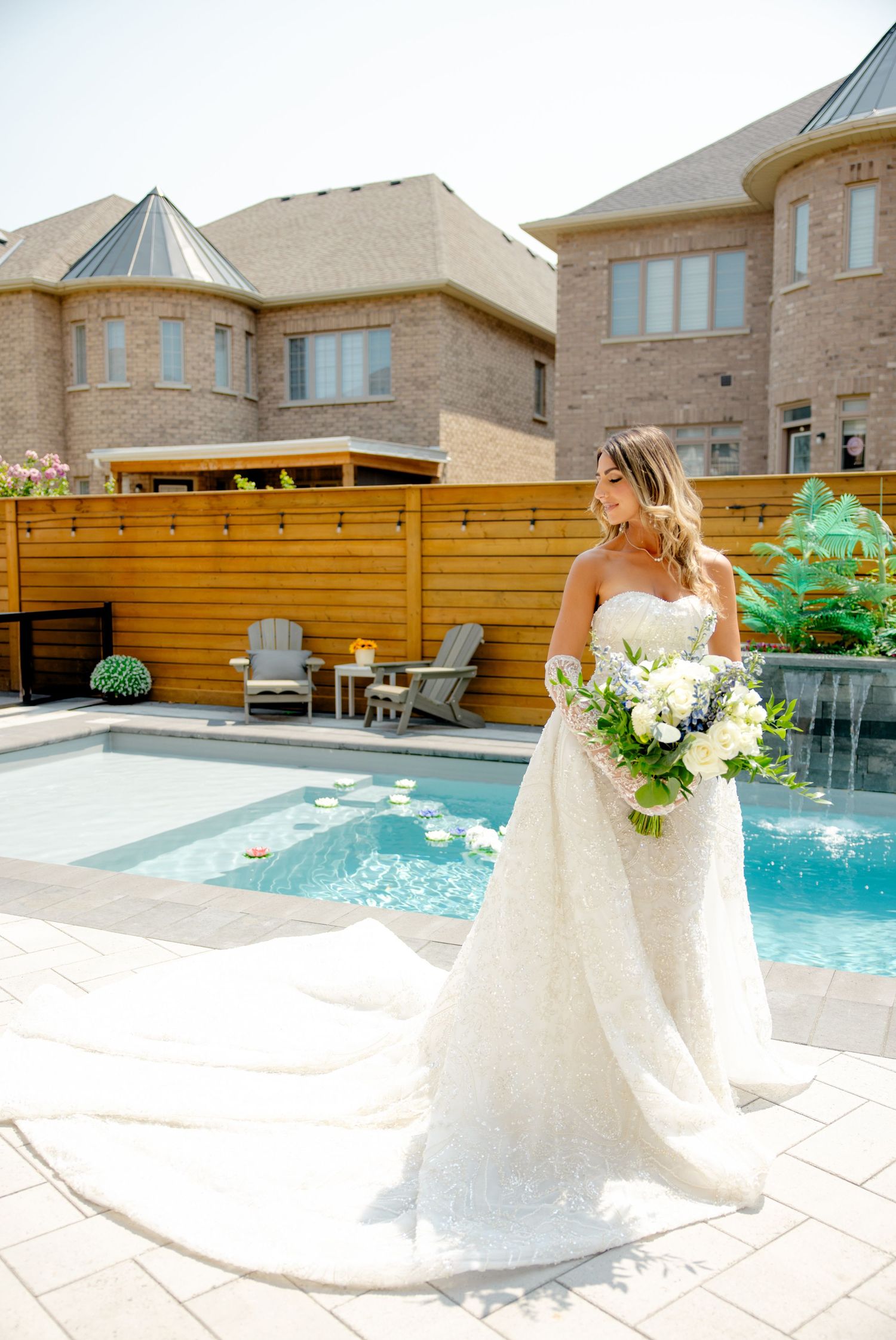 Wedding portrait featuring a white gown against modern poolside setting with brick mansion backdrop.