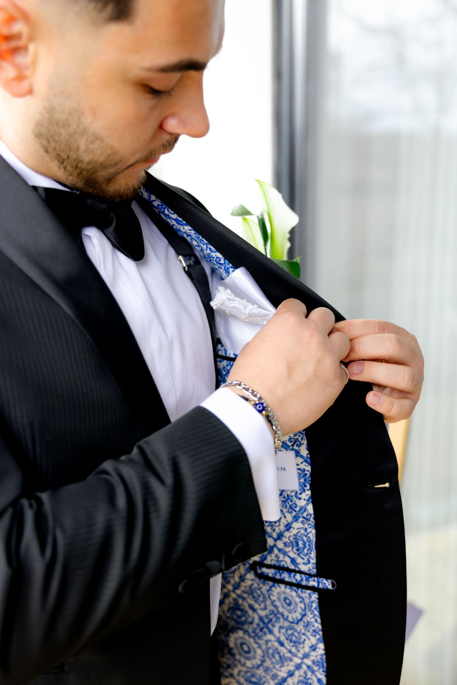 Close-up of a blue patterned tie being adjusted with boutonniere.
