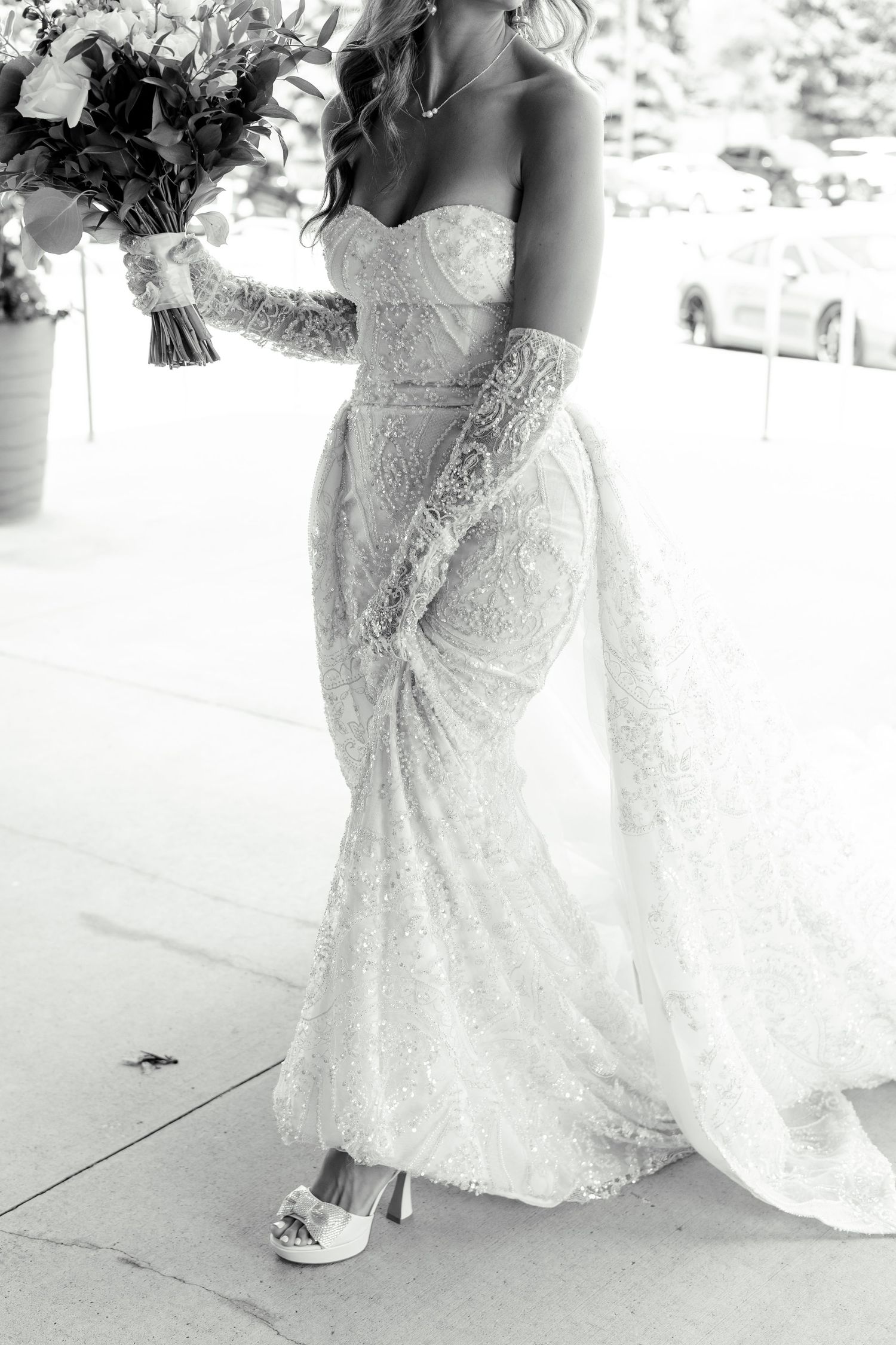 A detailed black and white photo showcasing an intricate lace wedding dress with a fitted silhouette.