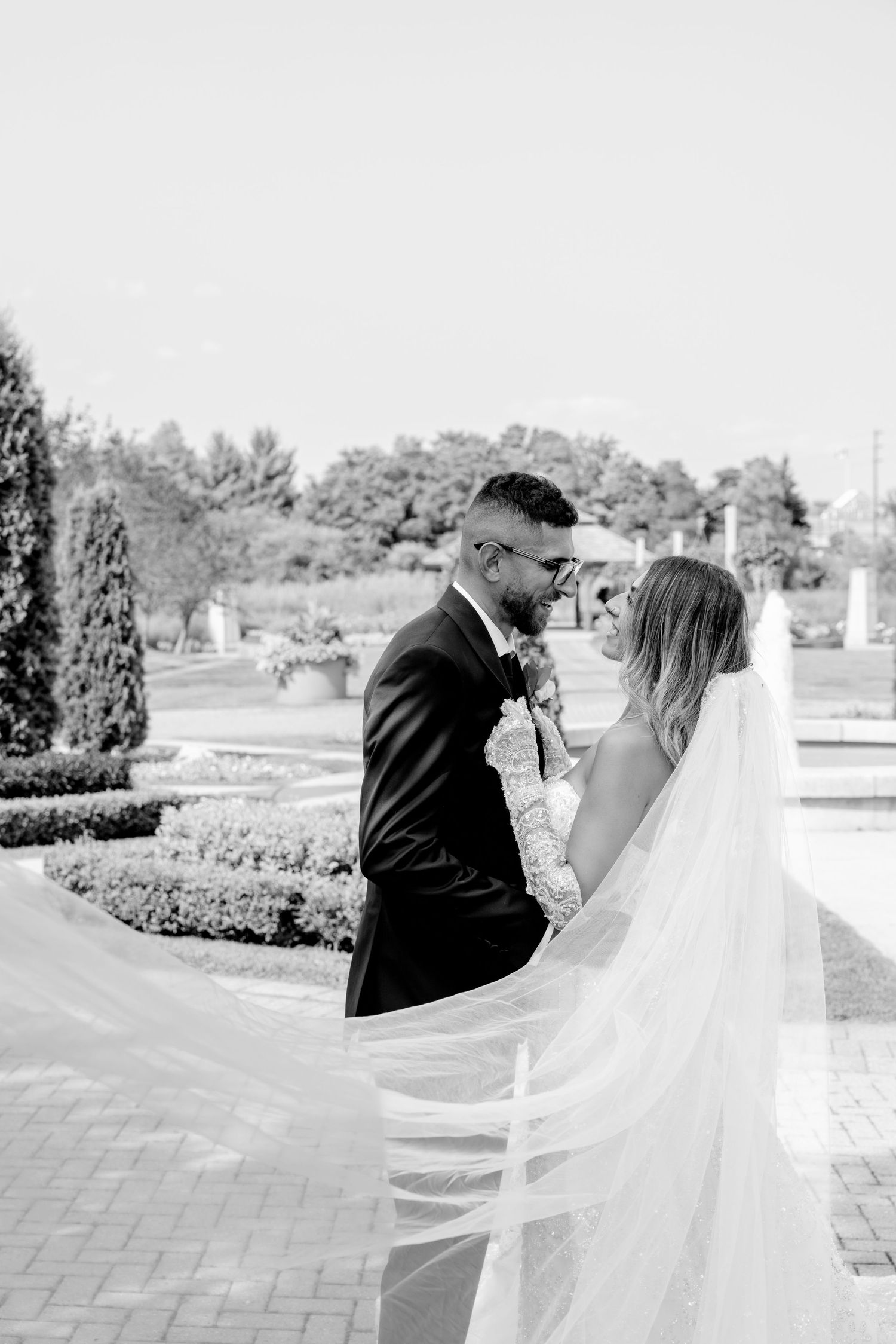 Black and white wedding portrait shows couple sharing tender moment on brick pathway.