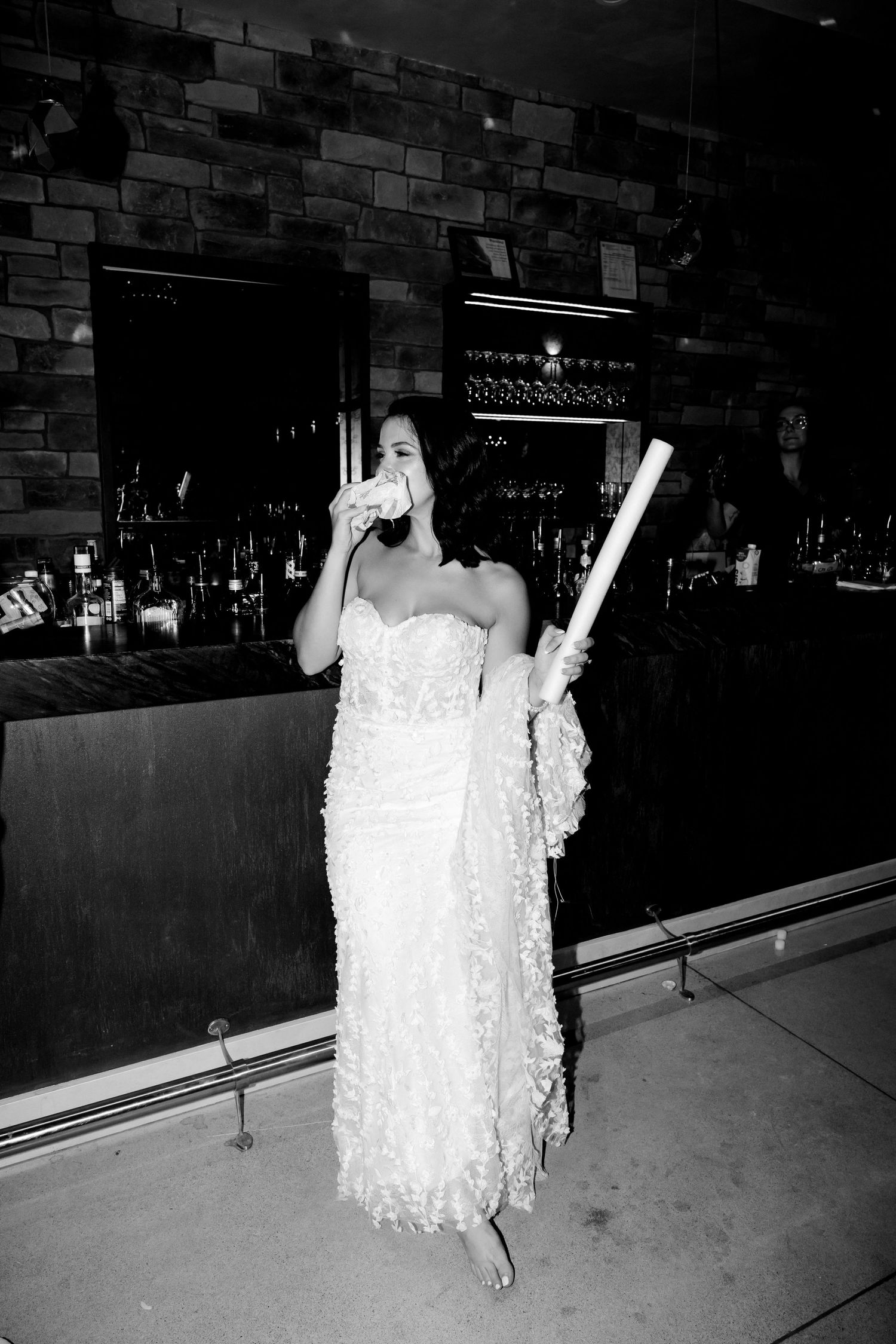 A person in wedding dress standing at bar counter holding light-colored objects.