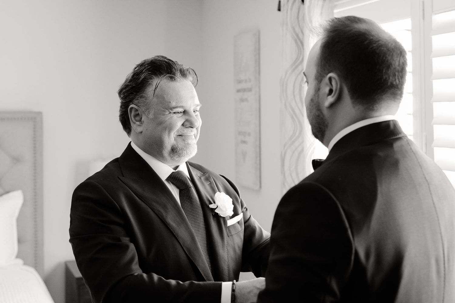 Two men in formal black suits engaged in conversation in a bright indoor setting.