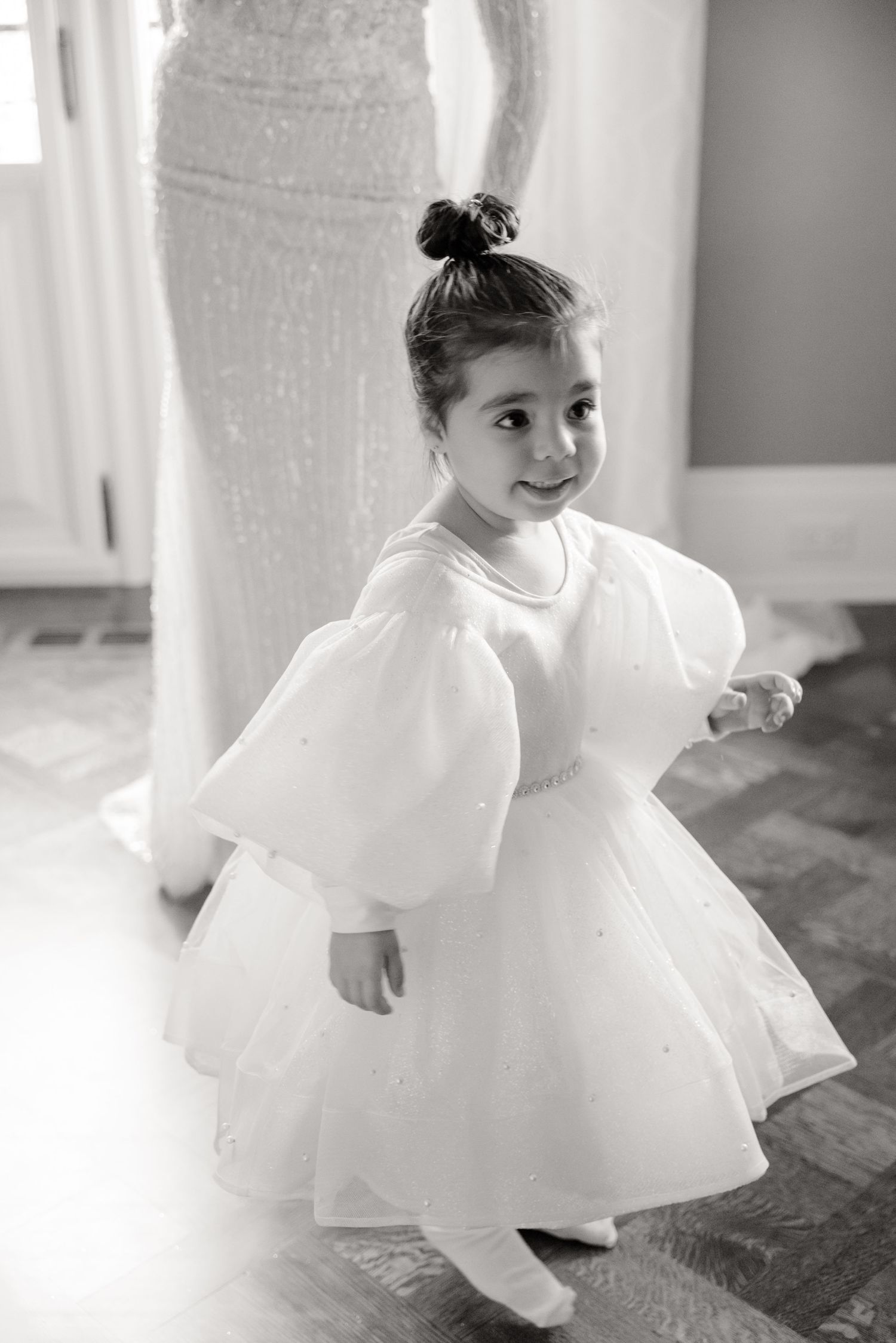 A young attendant twirls in a white dress with puffy sleeves during a wedding.