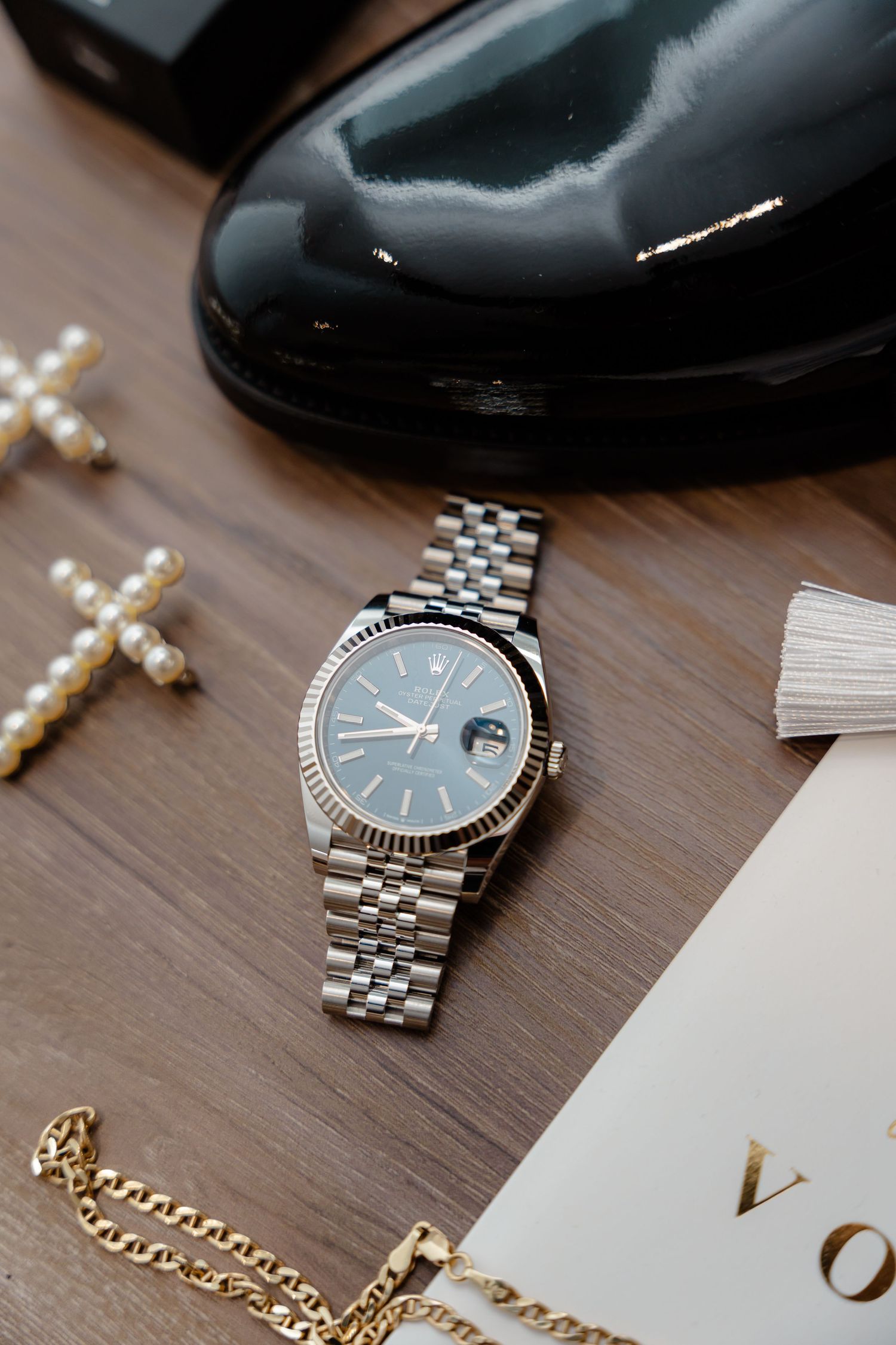 Luxury silver watch with pearl crosses and vows card on wooden surface.