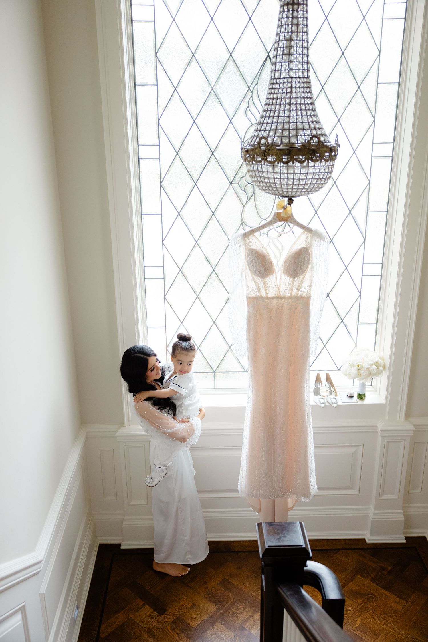 Blush wedding gown displayed beneath chandelier while someone admires it from below.