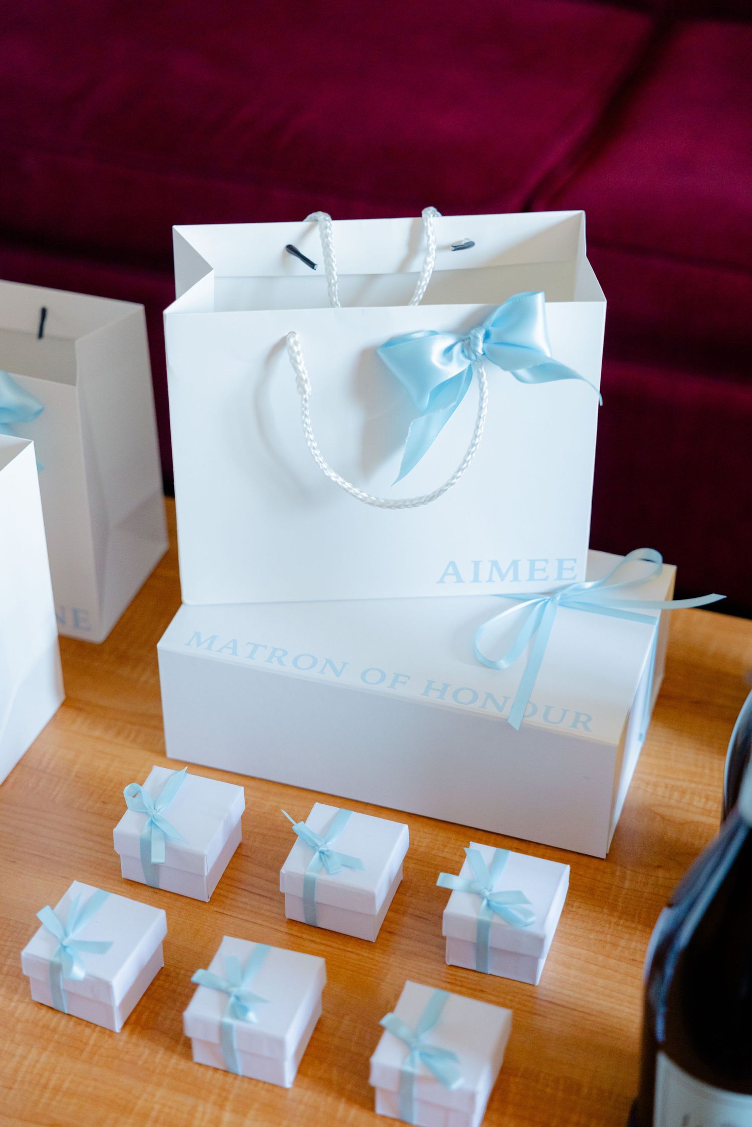White gift bags with light blue ribbons and small favor boxes arranged on wooden surface.