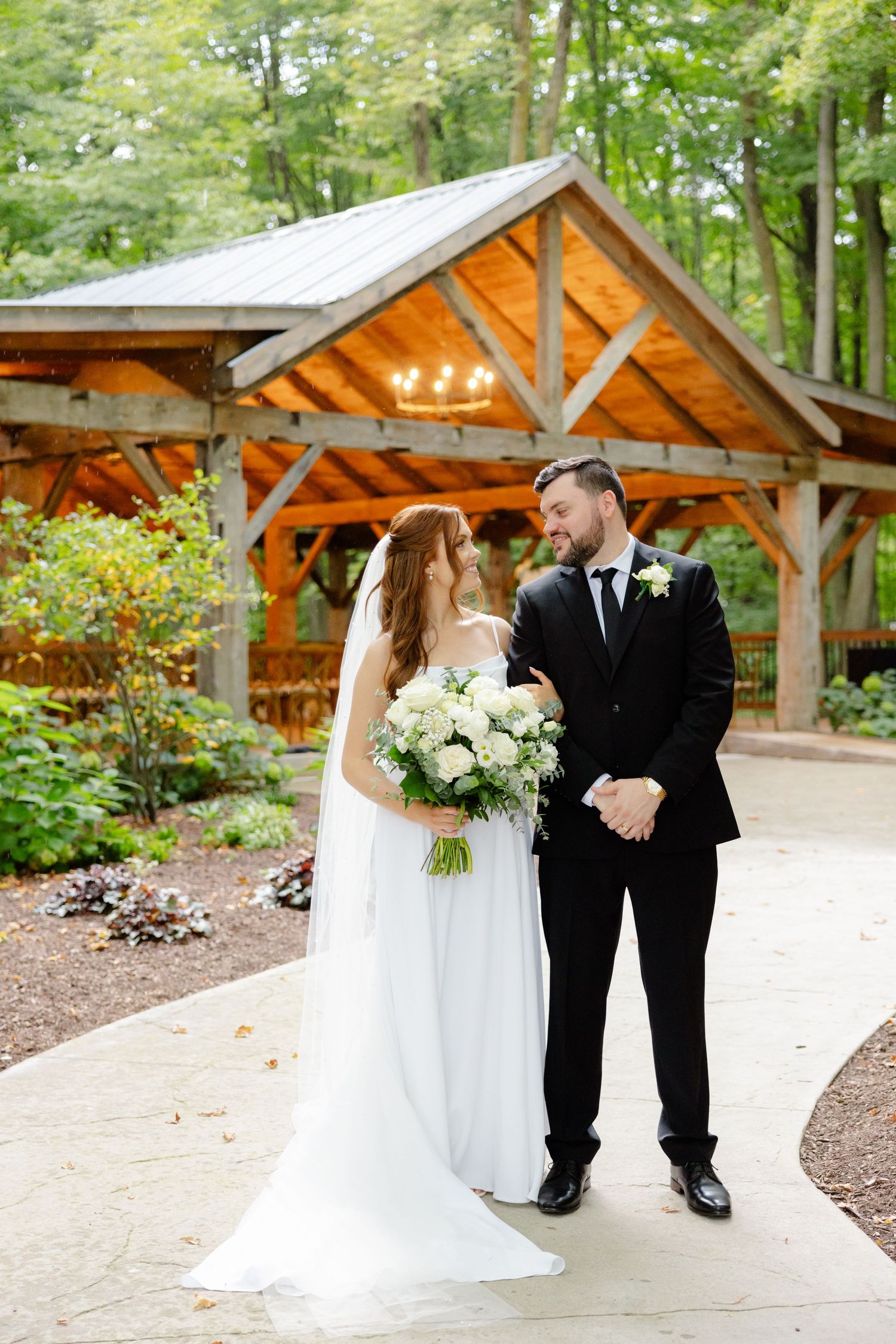 Wedding couple shares intimate moment in front of rustic pavilion with warm lighting.