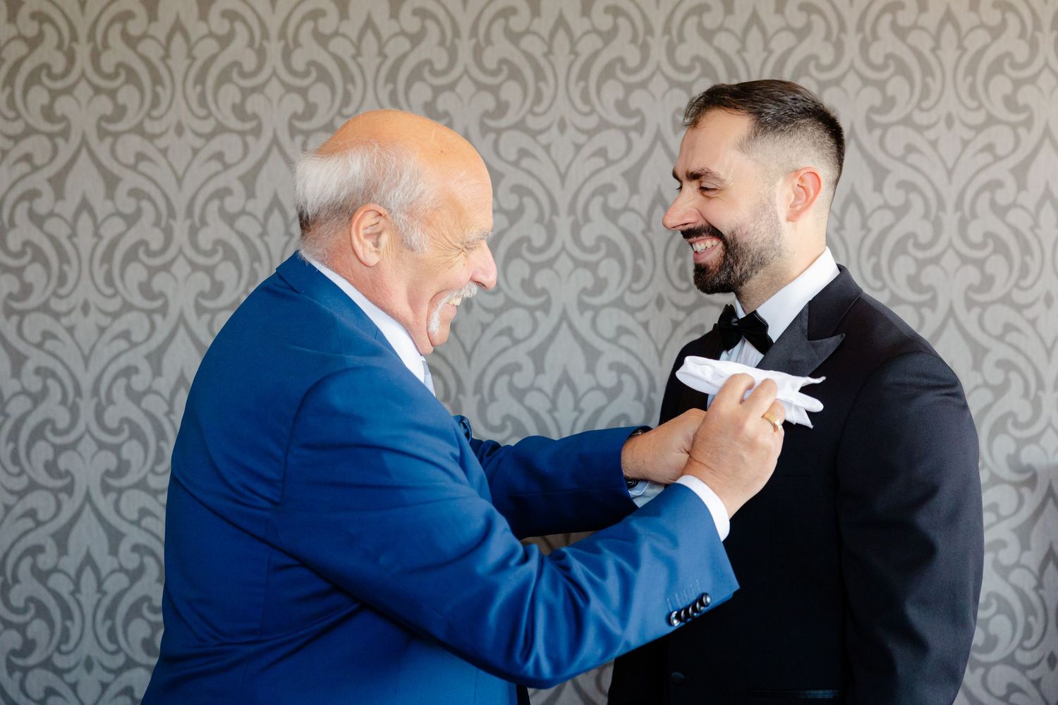 A heartwarming moment of formal attire adjustment between generations at a wedding.
