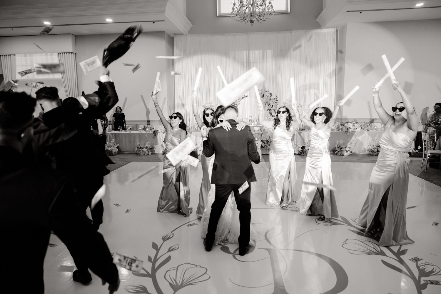 Black and white photo of wedding reception guests dancing and celebrating with raised arms.