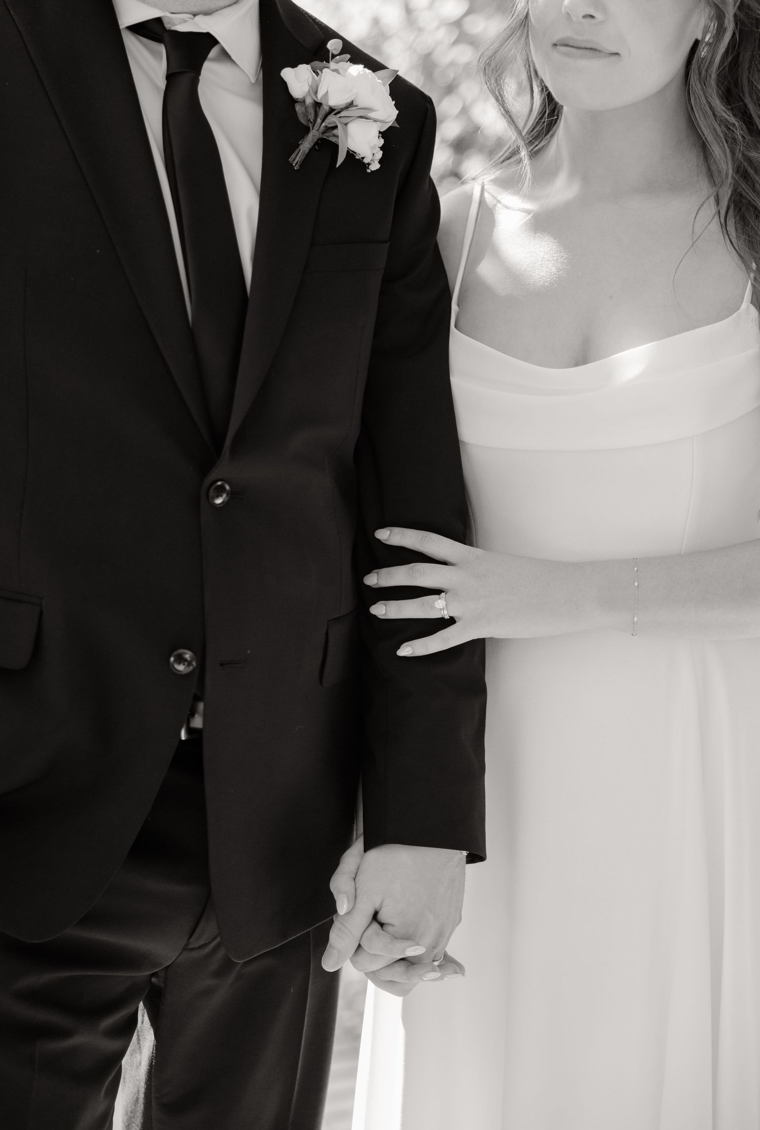 A black and white artistic photo showing details of wedding attire and tender embrace.