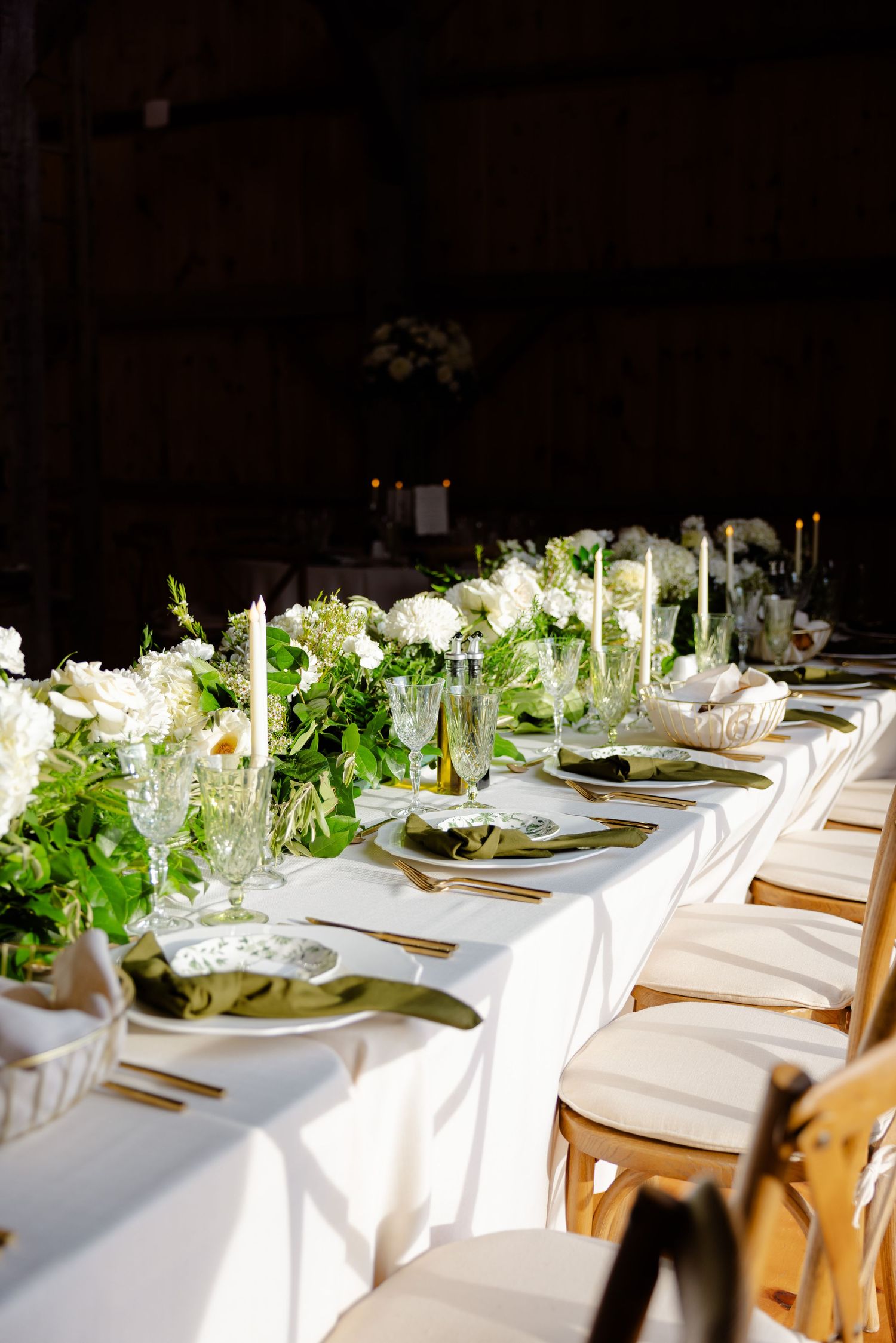 Sunlit wedding table with white linens, gold flatware, and lush greenery centerpieces.