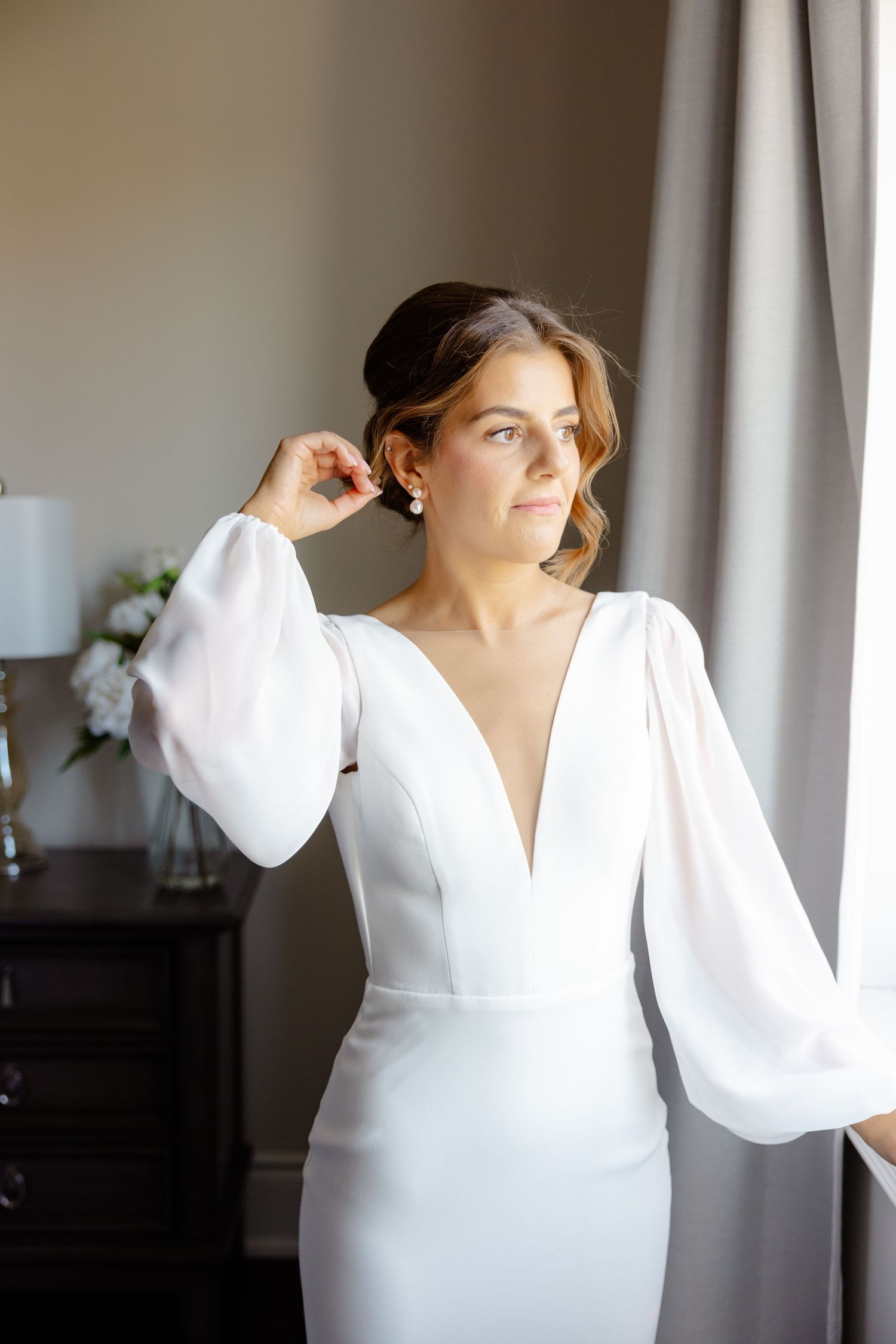 Modern wedding dress with statement balloon sleeves and deep v-neckline captured in natural window light.