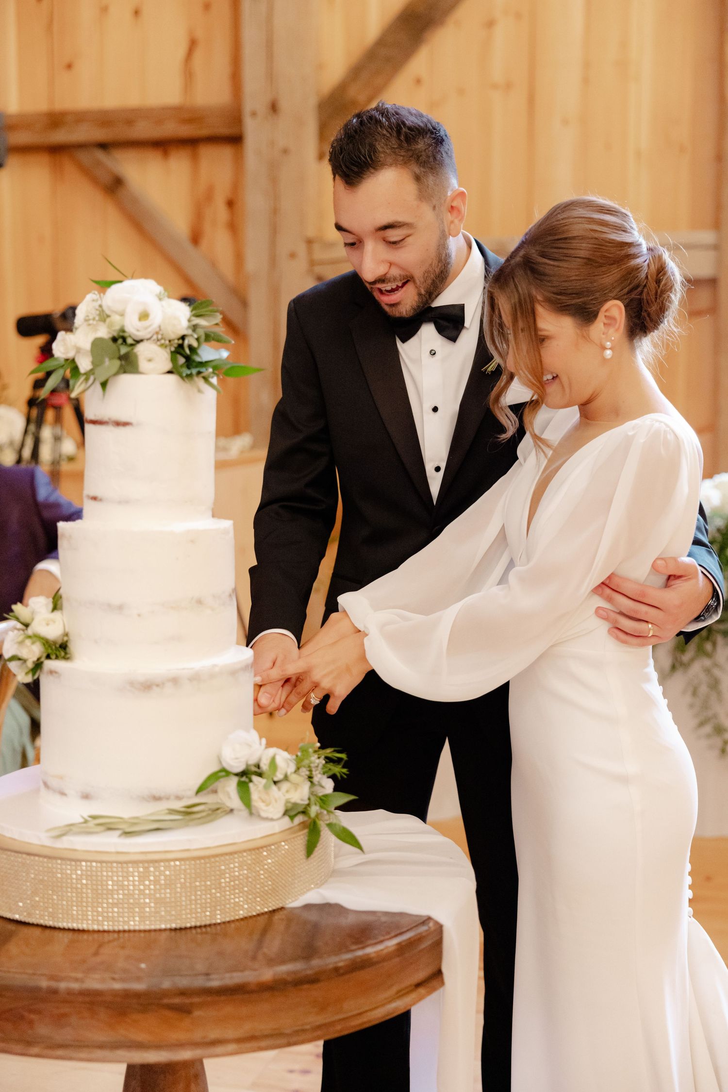 Newlyweds share a joyful moment while cutting their white tiered wedding cake.