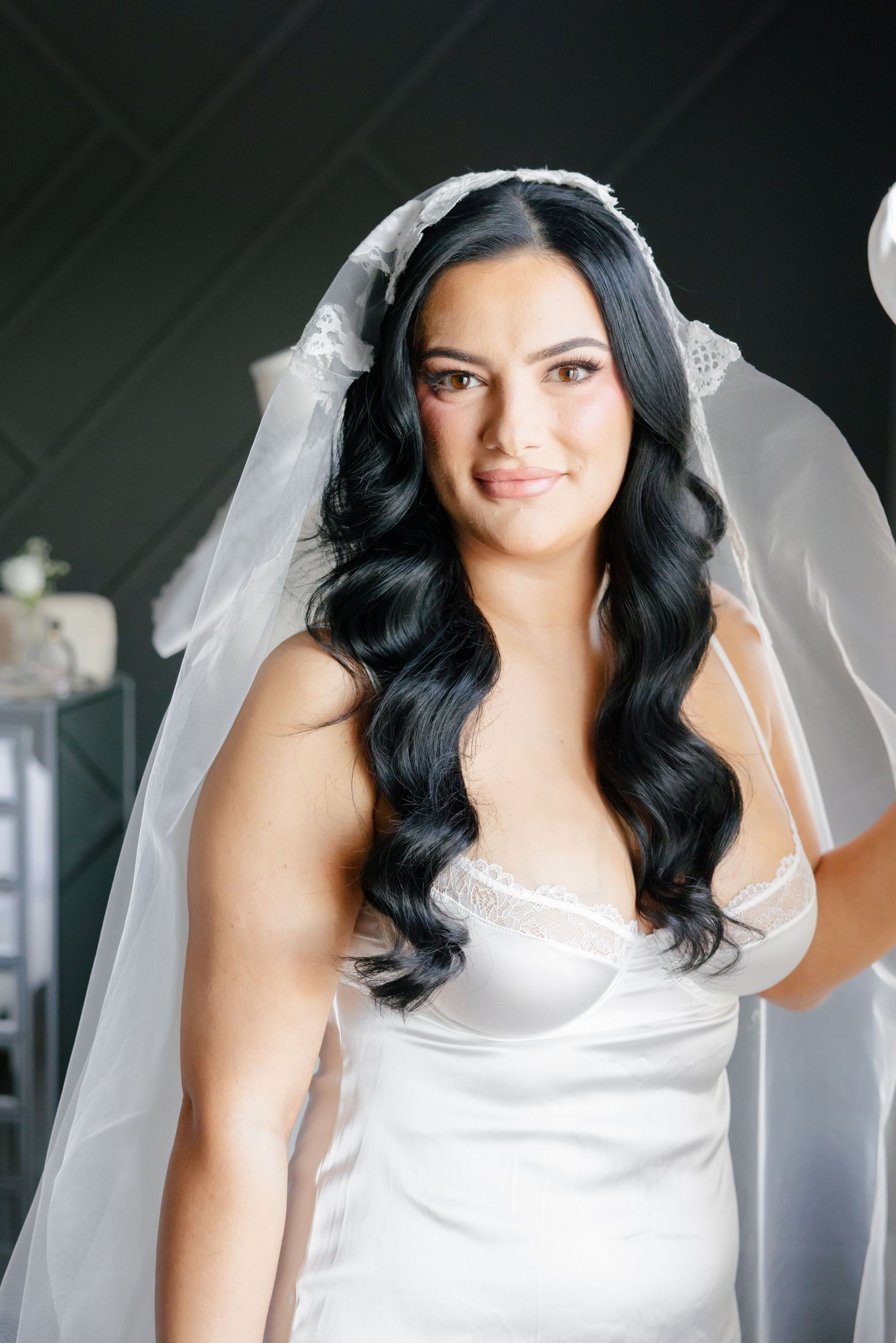 Bride in a classic white wedding gown with flowing dark waves and cathedral veil.
