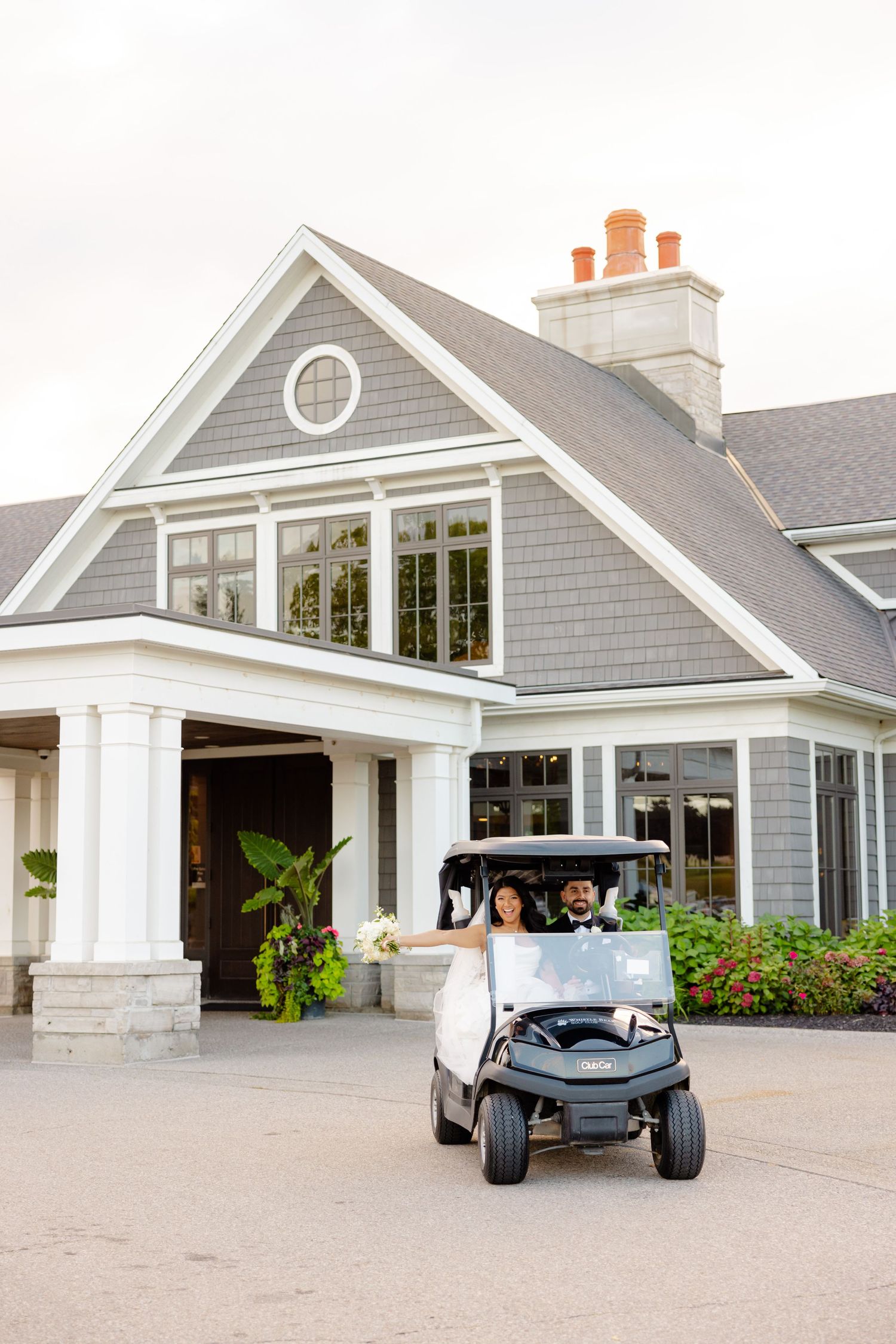 A golf cart parked in front of a gray coastal-style house with white trim and columns.