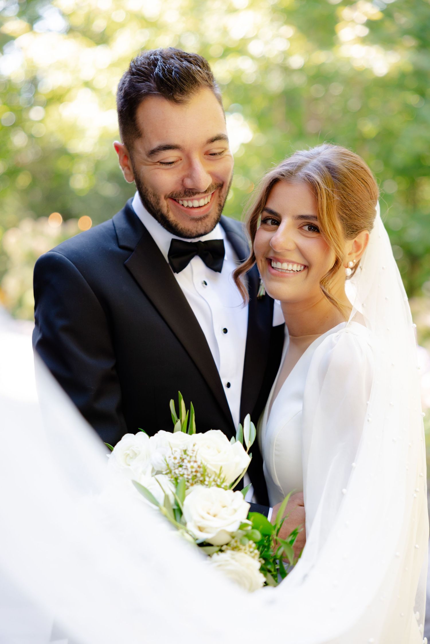Candid wedding photo showing genuine laughter between couple with white floral accents.