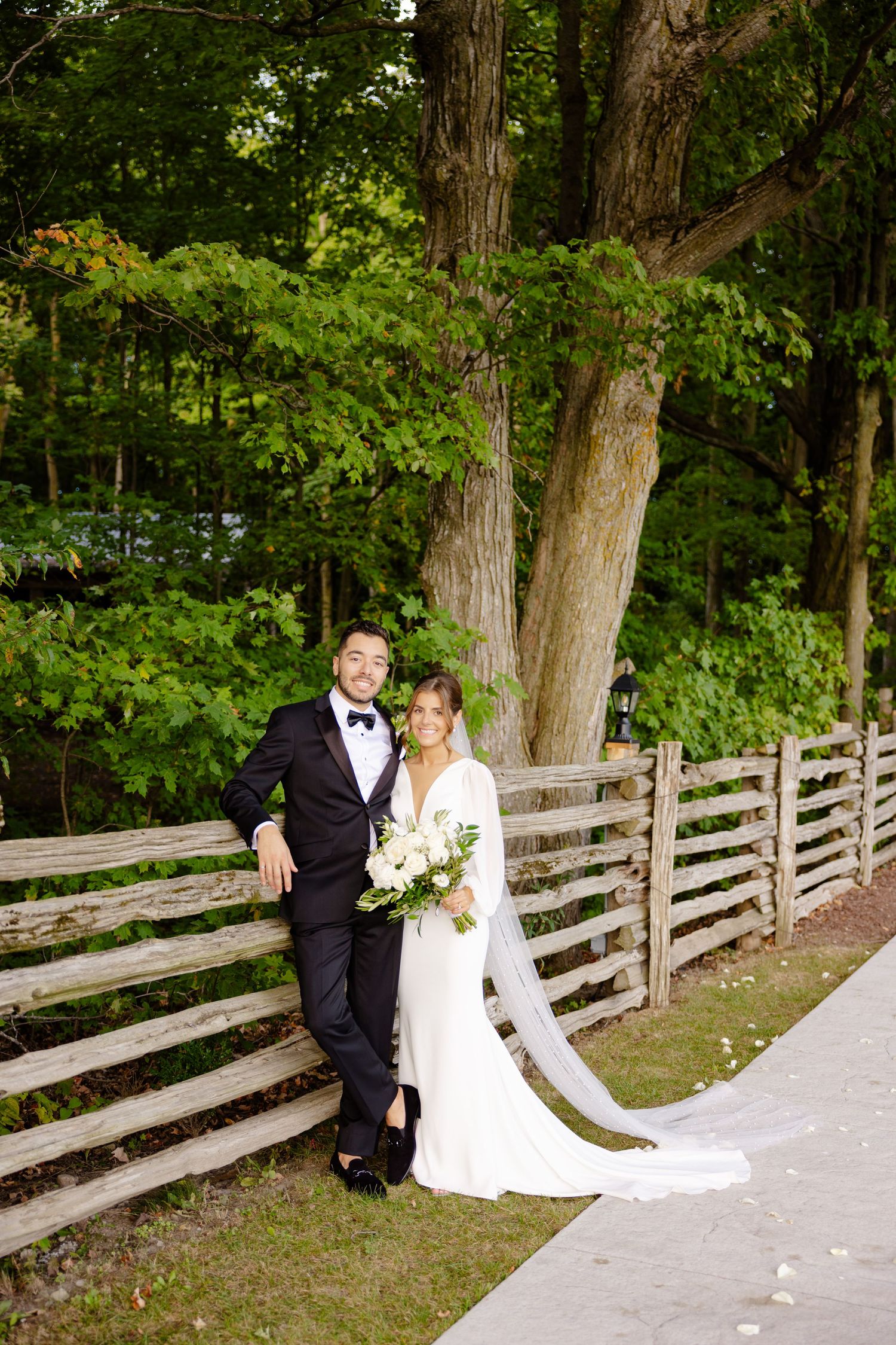 A wedding portrait by a wooden fence with the couple in elegant formal attire.